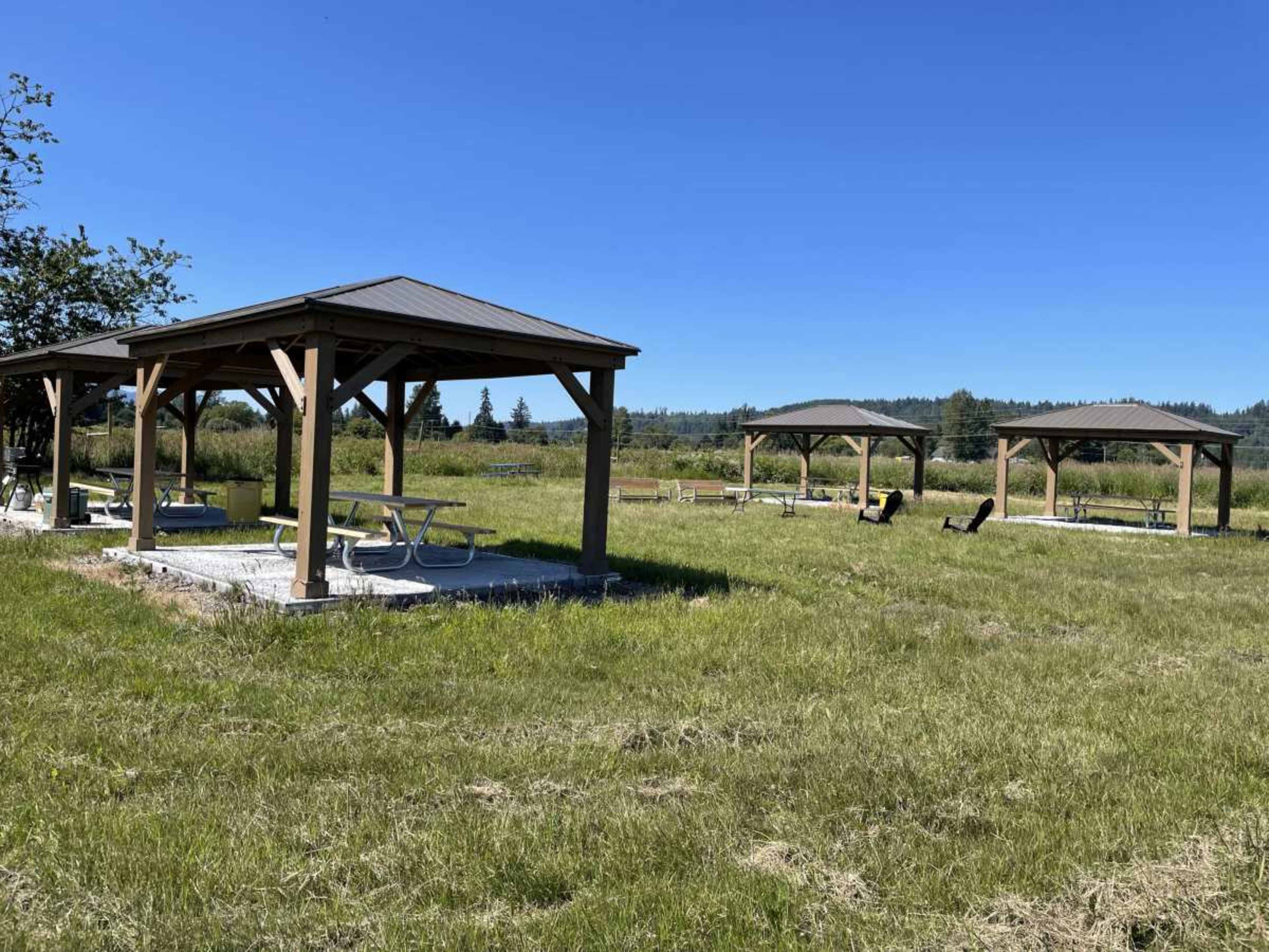 Several wooden picnic pavilions set on a grassy field under a clear blue sky.