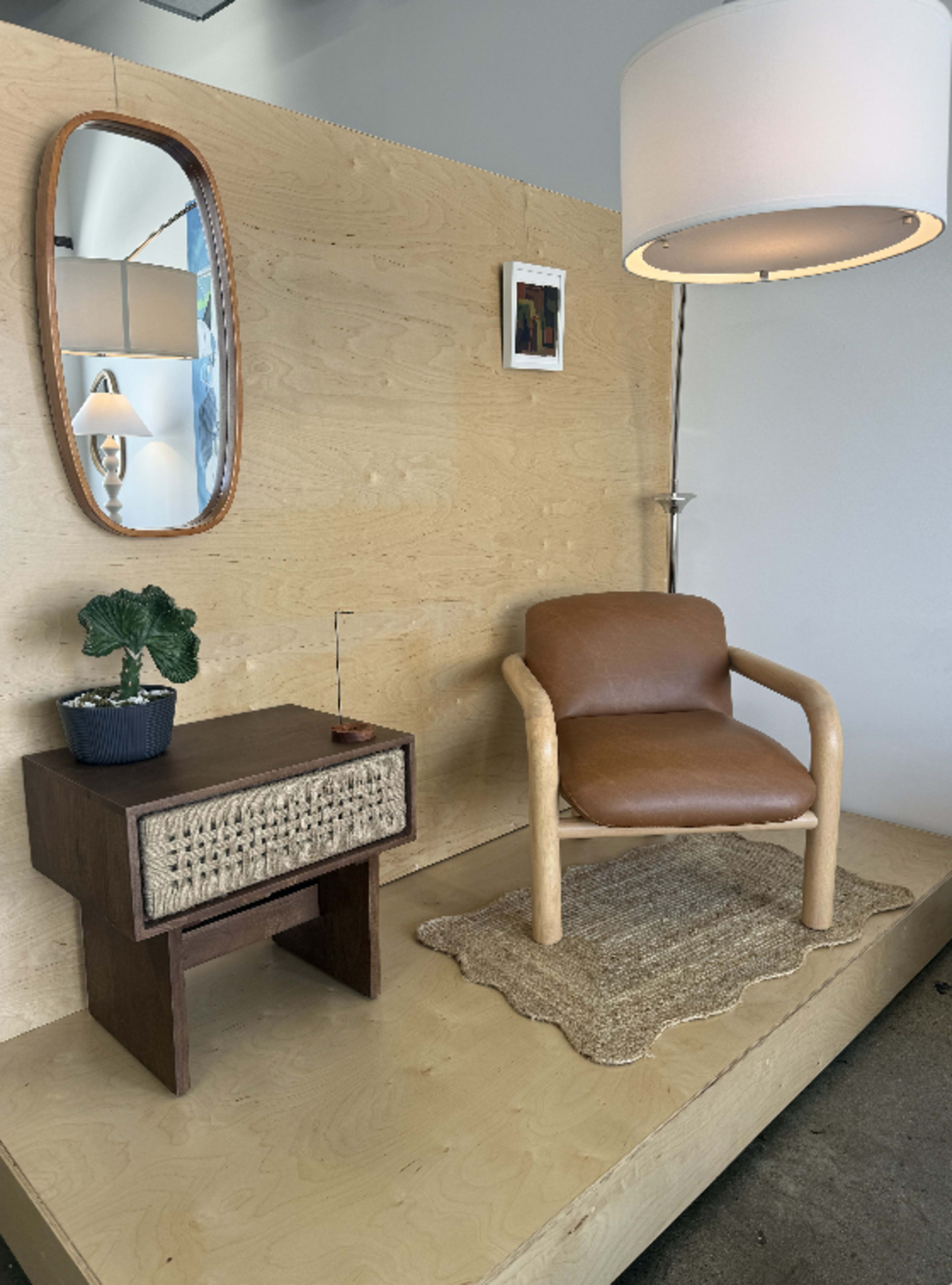 The image features a minimalist interior scene with a wooden wall, a modern chair, a small side table, a lamp, a potted plant, and a mirror.