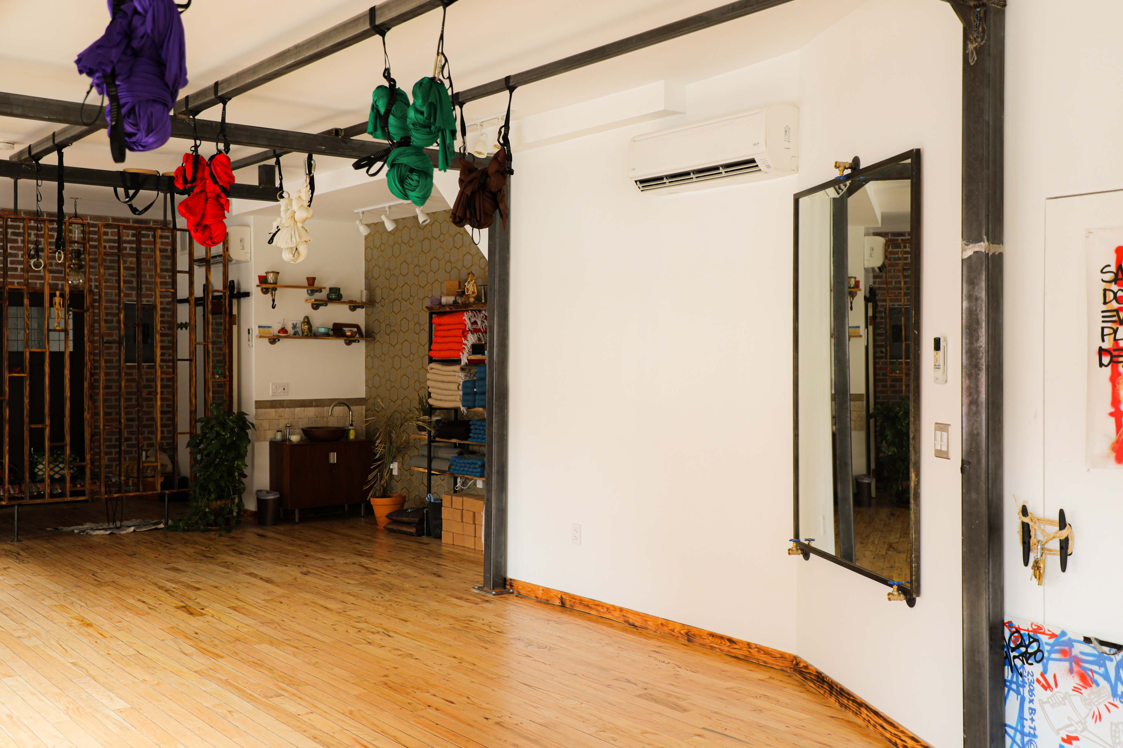 The room features wooden flooring, mirrored walls, and suspended fabric for aerial activities, with shelves and a sofa along the sides.