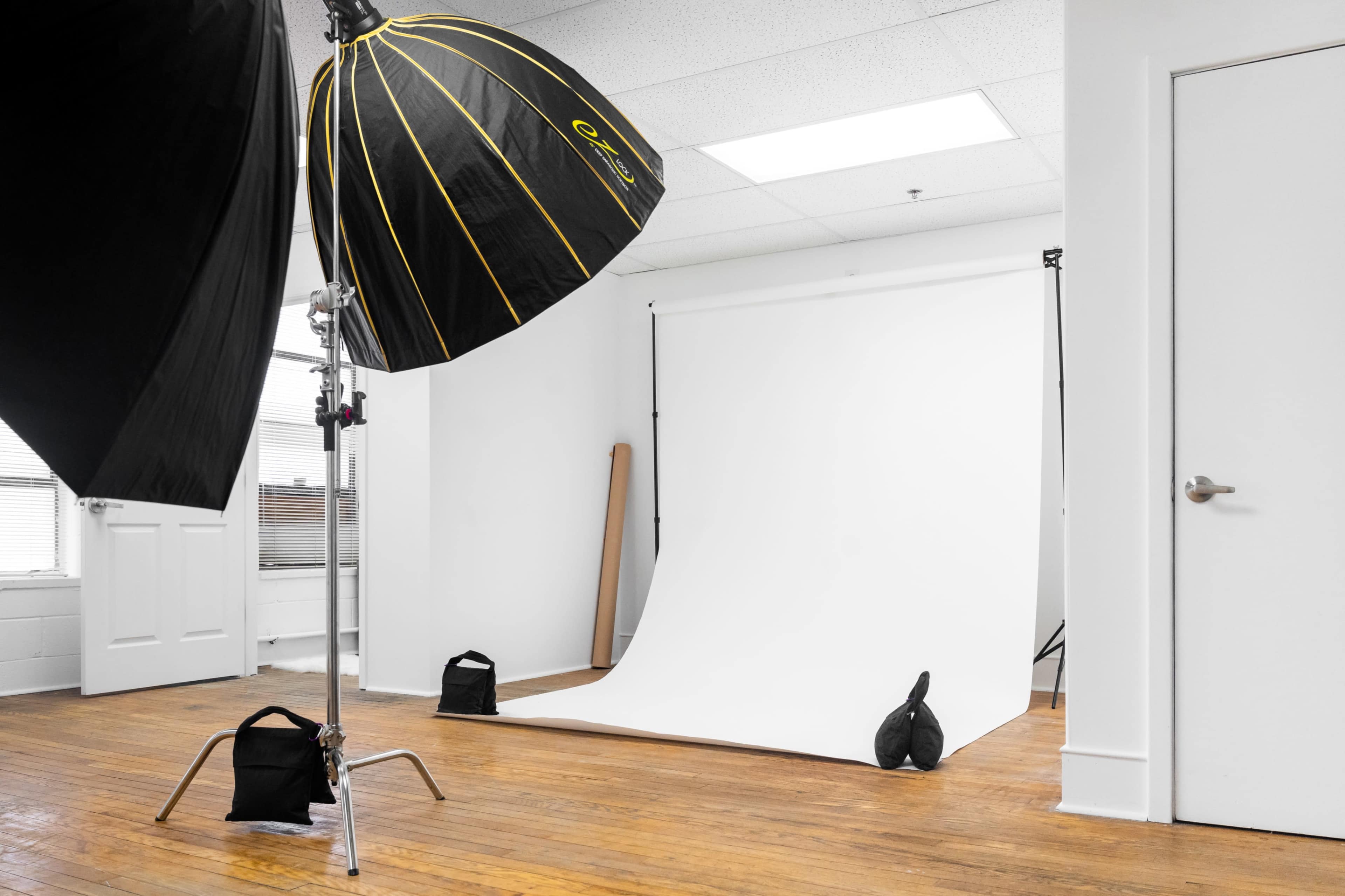 A photography studio featuring a white backdrop, lighting equipment, and wooden flooring.