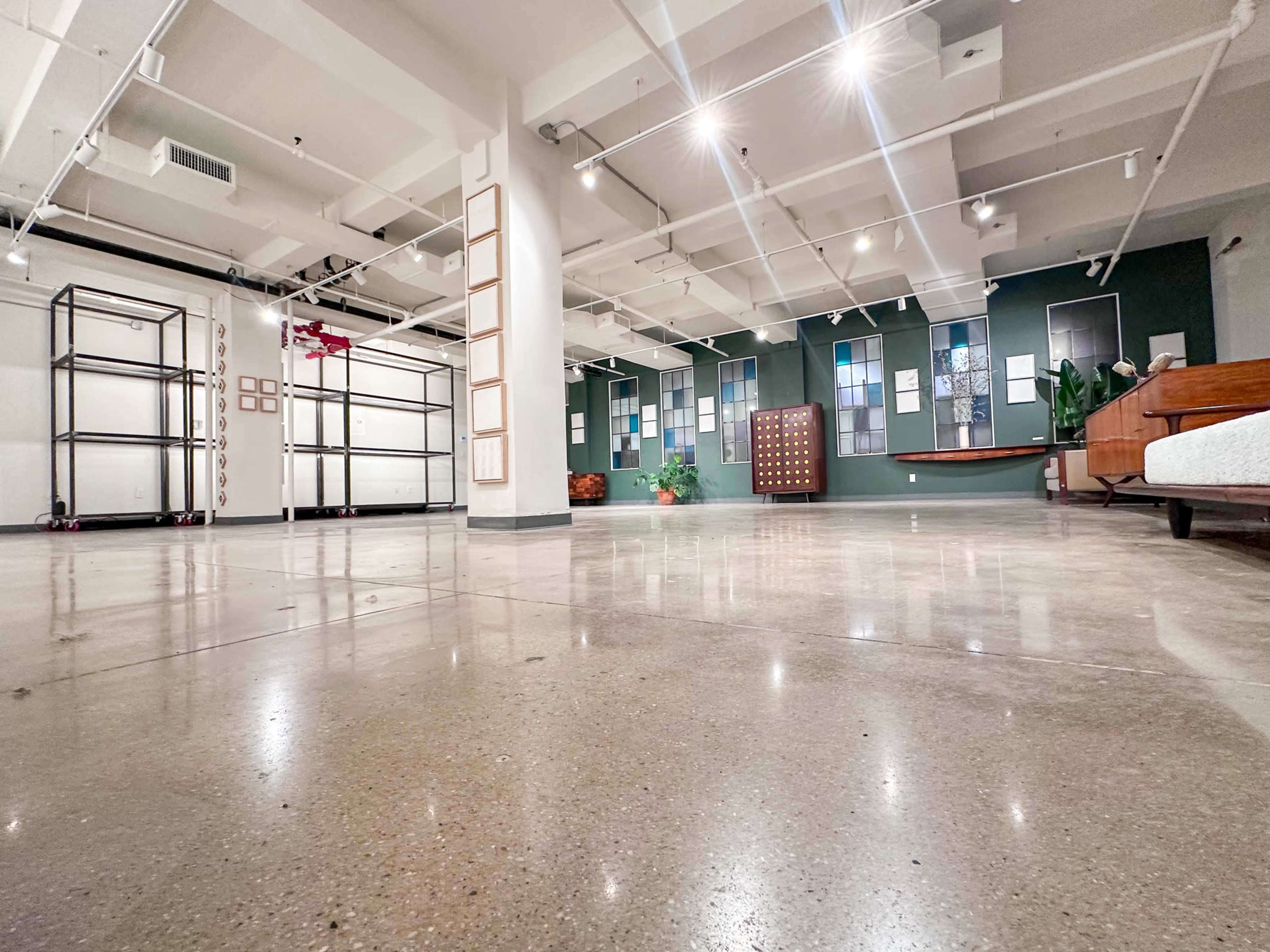 The image shows a spacious, empty interior with polished concrete floors and sections of the walls featuring various frames and cabinets.