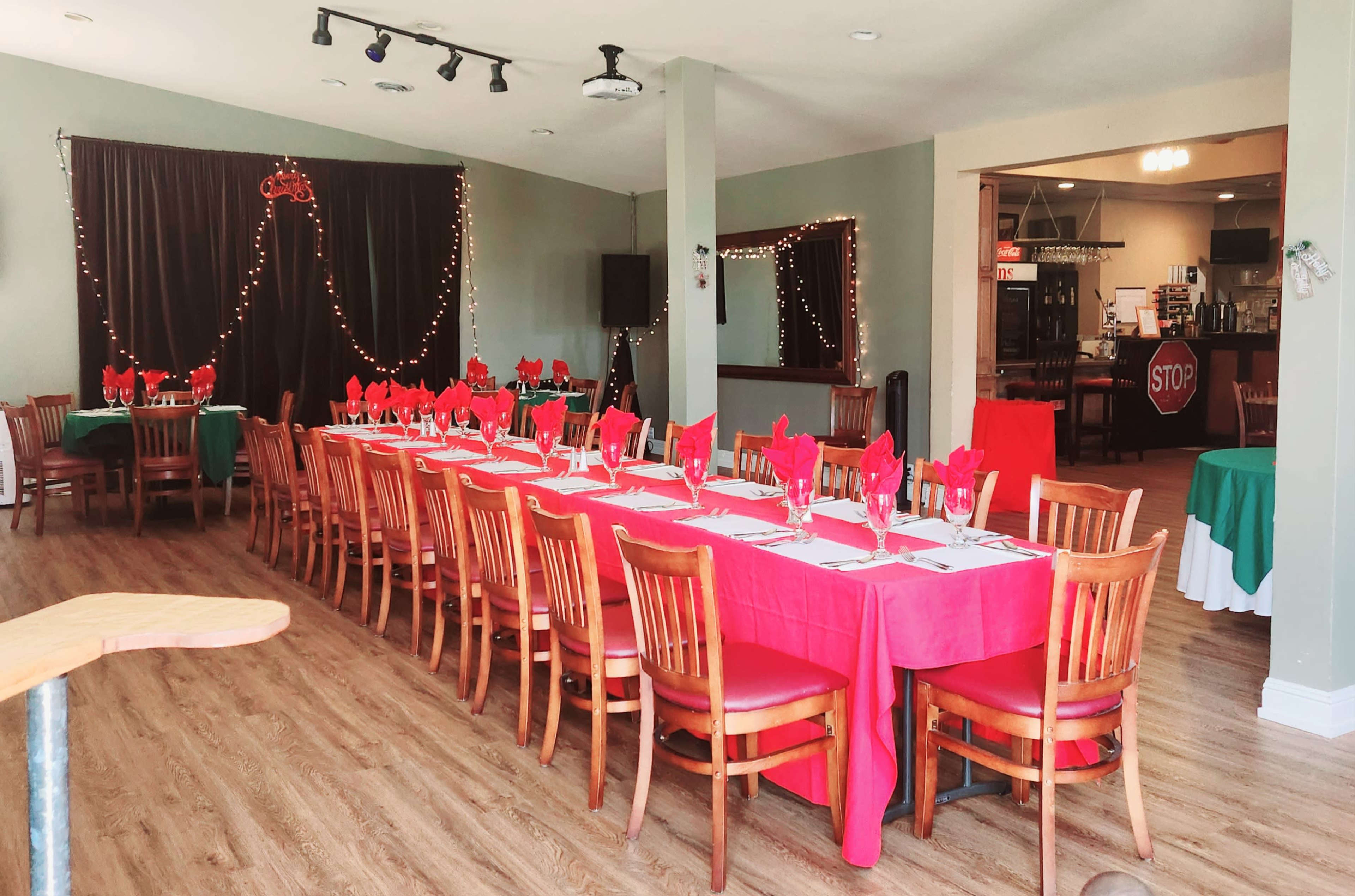A long table is set with red and white tablecloths and red napkins in a restaurant decorated with lights.