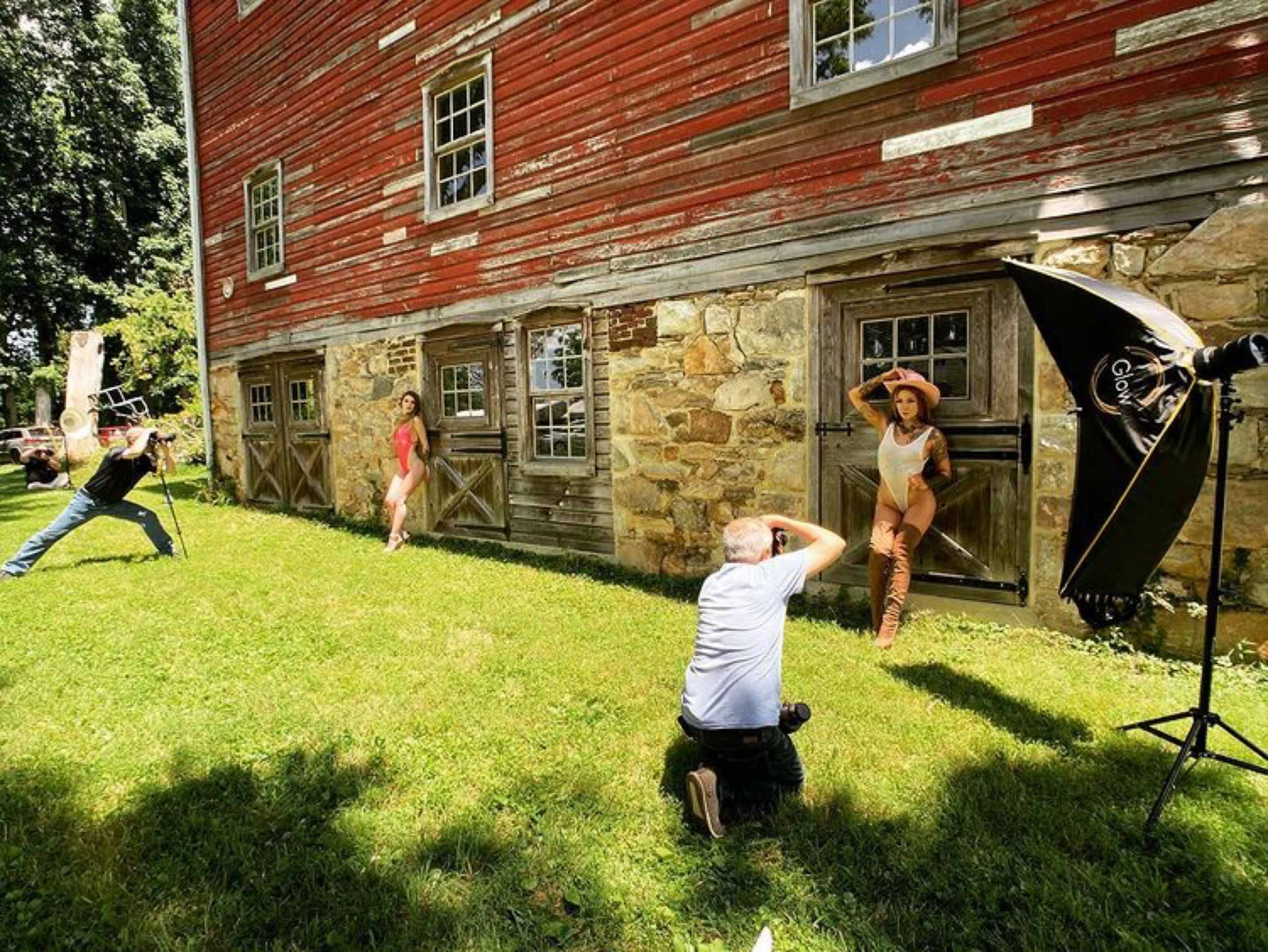A photographer captures models posing in front of a rustic barn while an assistant sets up lighting equipment.