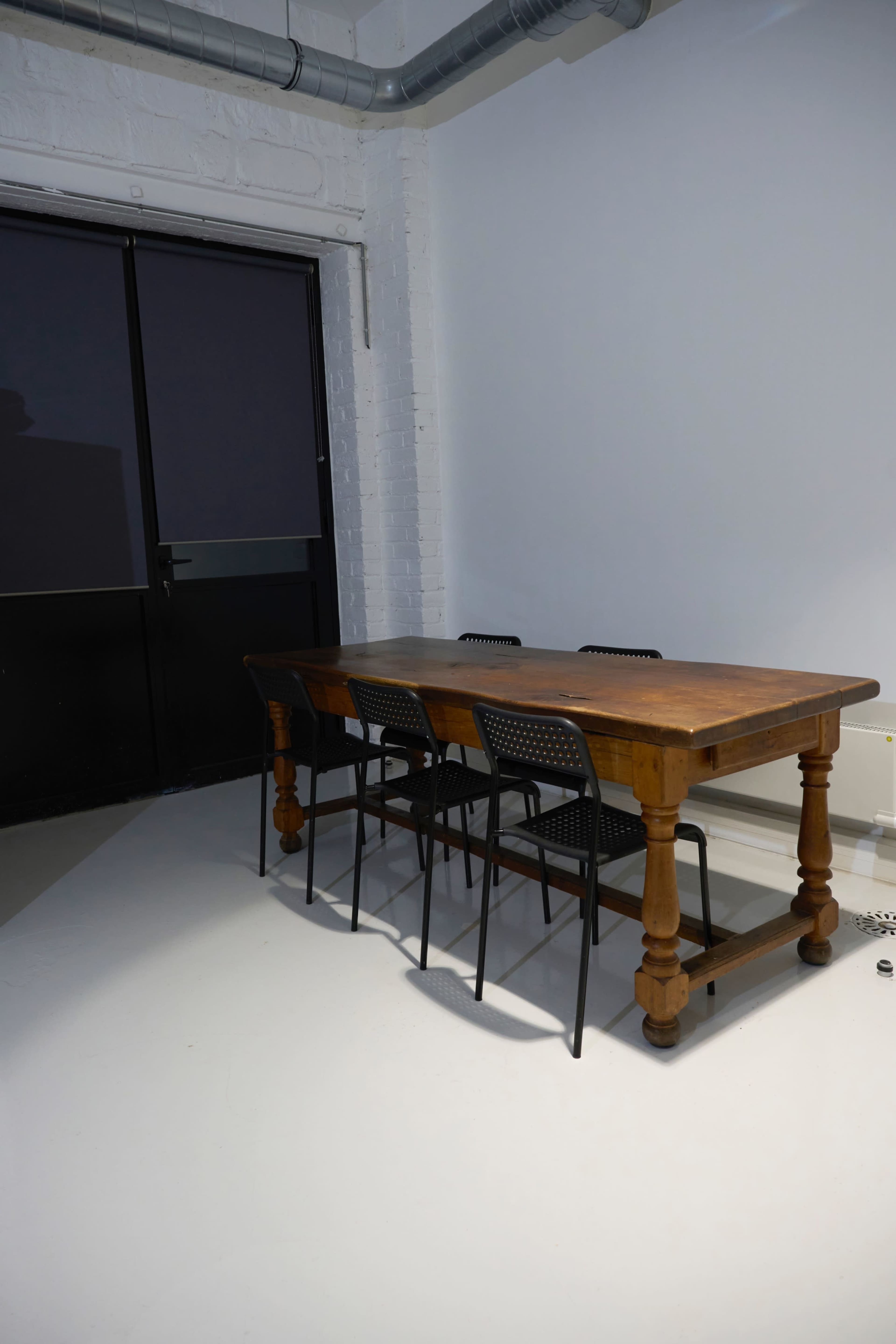 A wooden table with six black chairs is positioned against a white wall near a dark glass door.