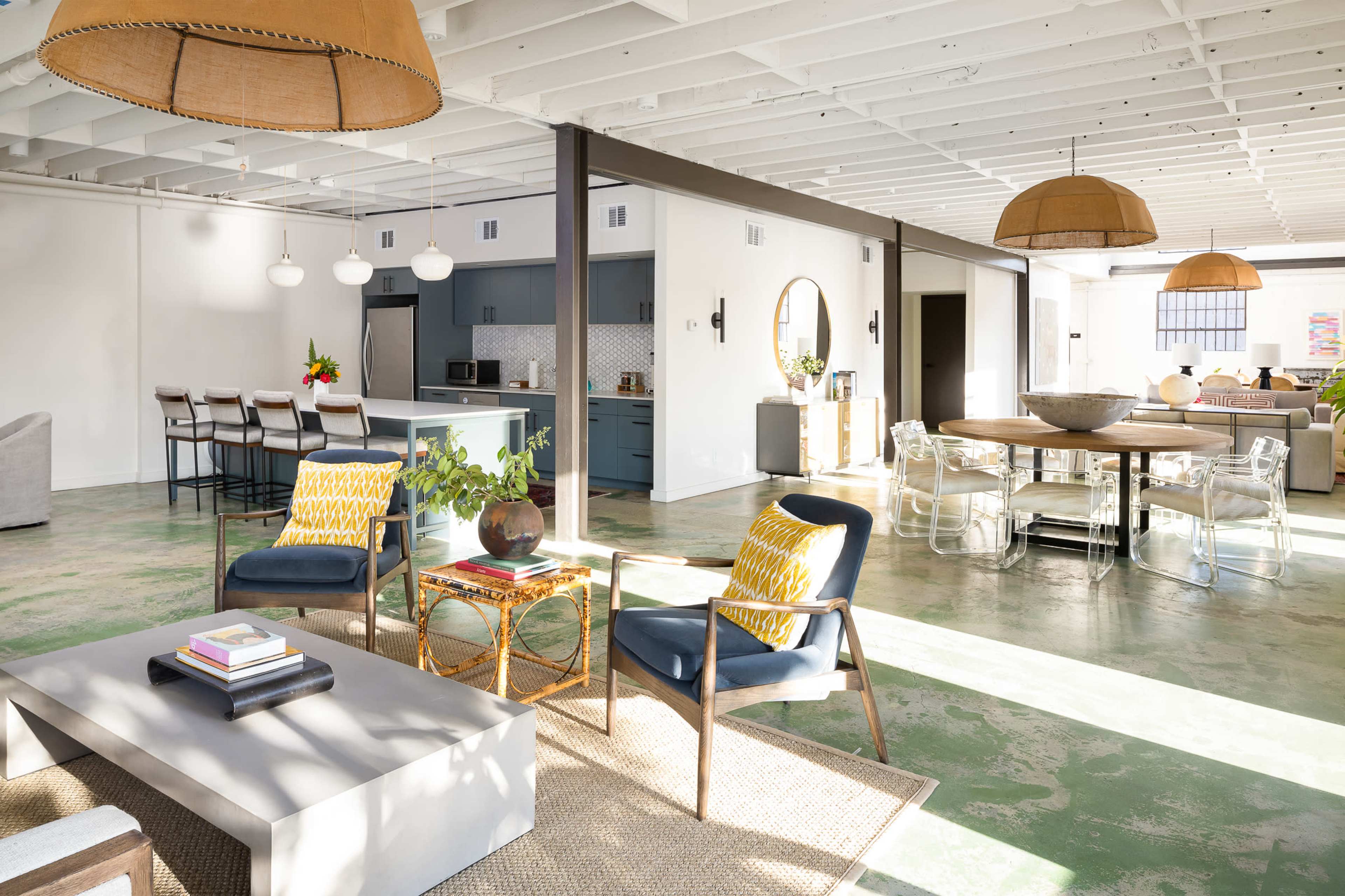 An open-concept interior space featuring a living area with modern furniture, a dining area with a round table, and a kitchen in the background.