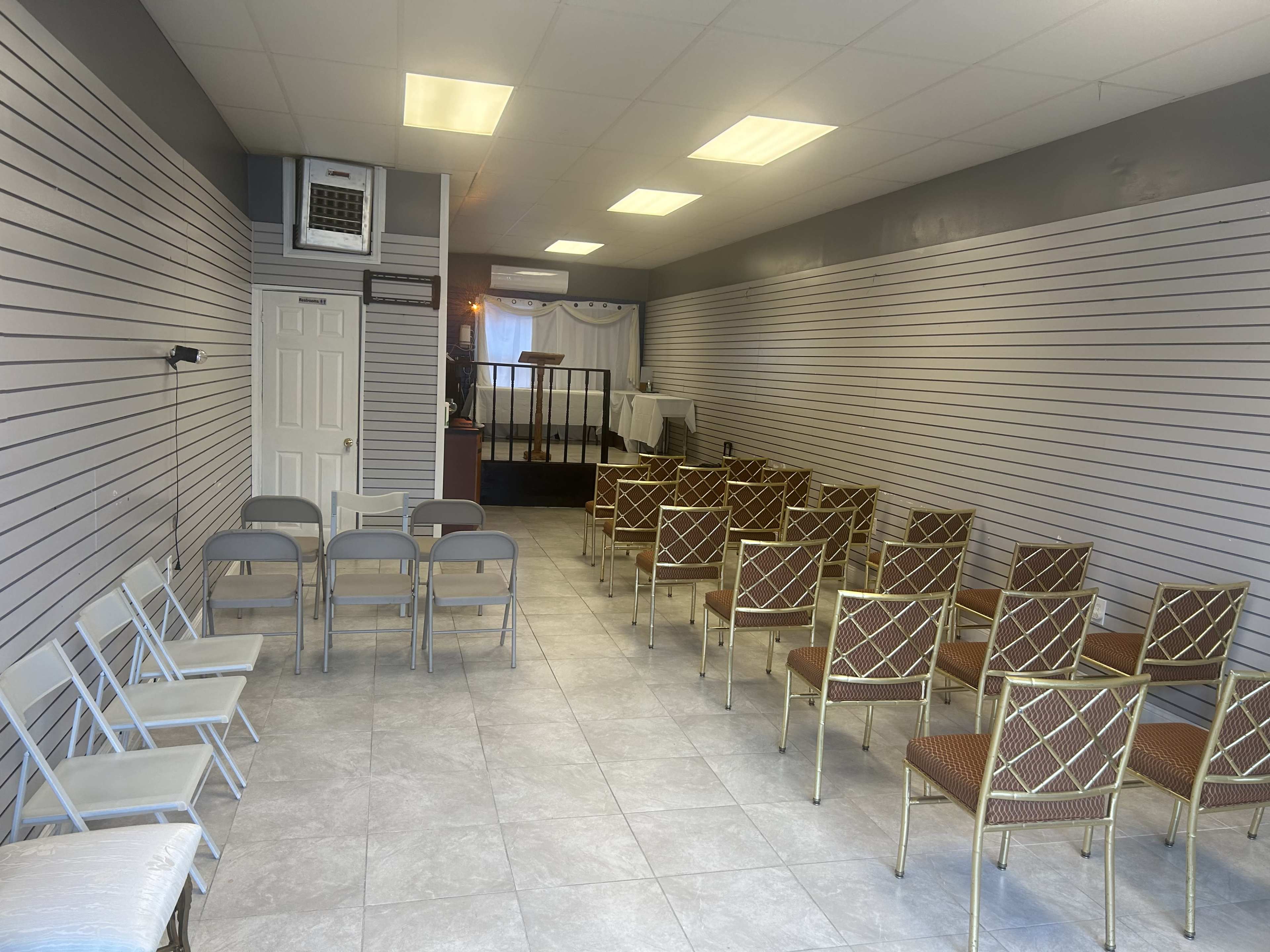 A spacious room with rows of chairs facing a small elevated stage at one end.