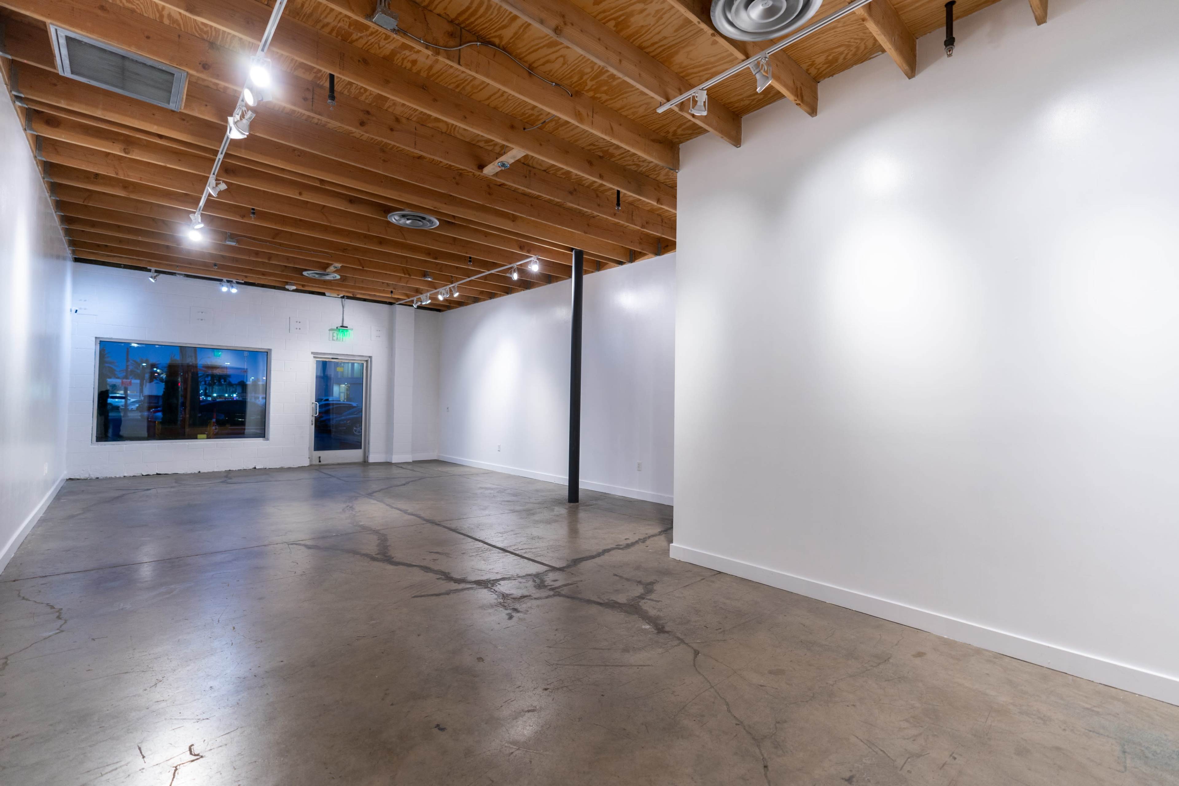 An empty interior space with polished concrete floors, wooden beams on the ceiling, and white walls.