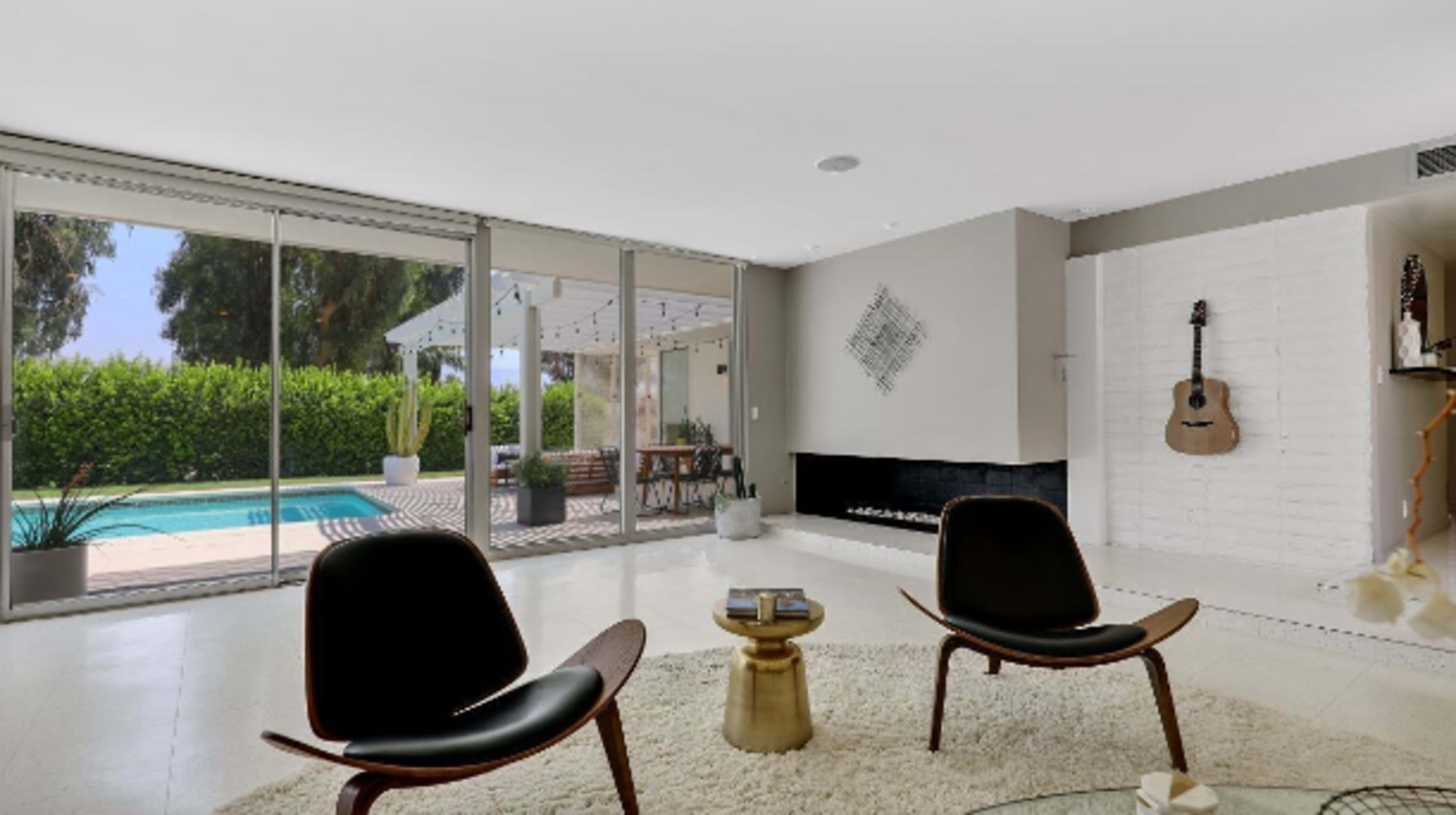 The image shows a modern living room with two black chairs facing a glass wall that overlooks a pool and outdoor patio.