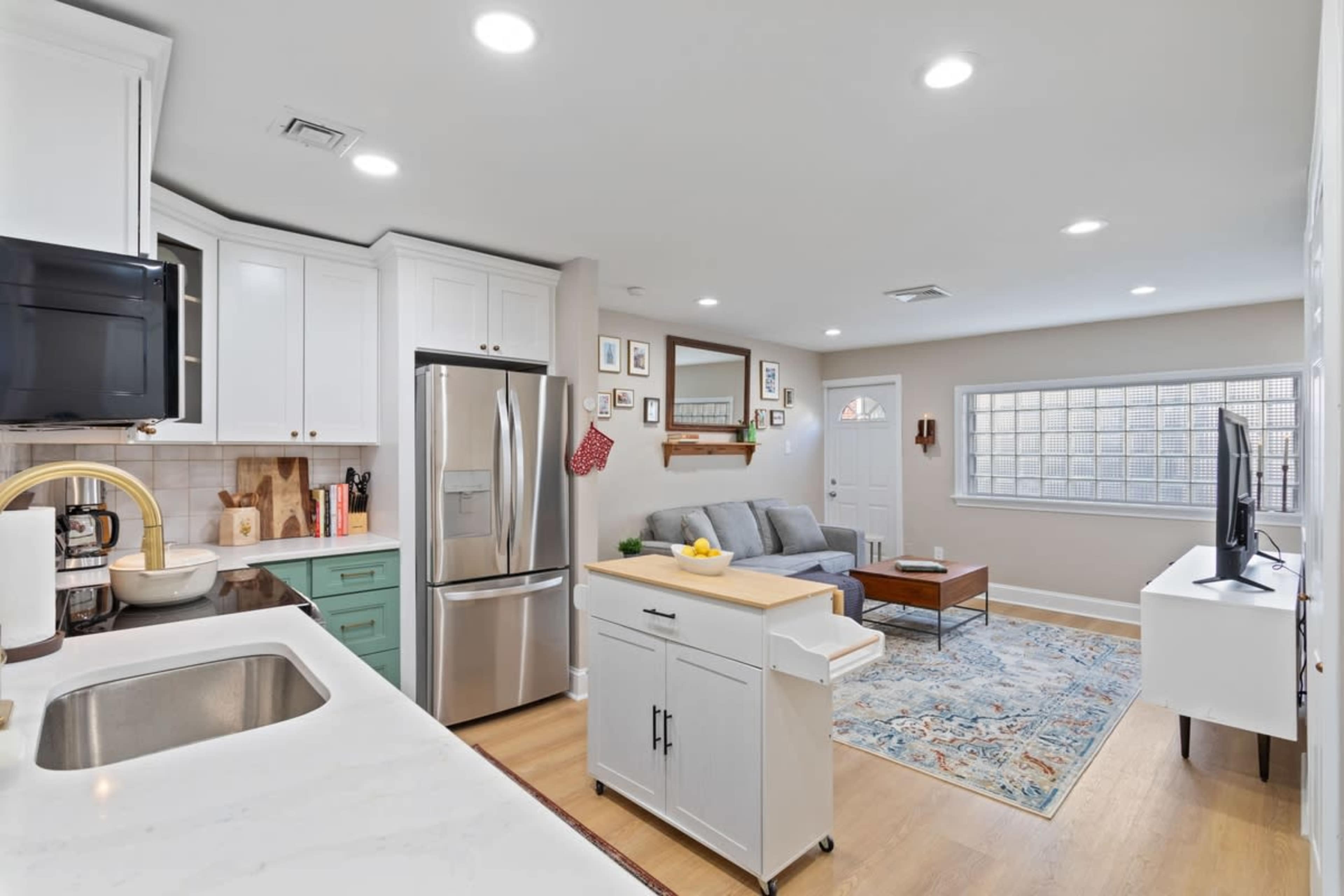 The image shows a modern kitchen and living area with white cabinetry, a gray sofa, and a wooden coffee table.