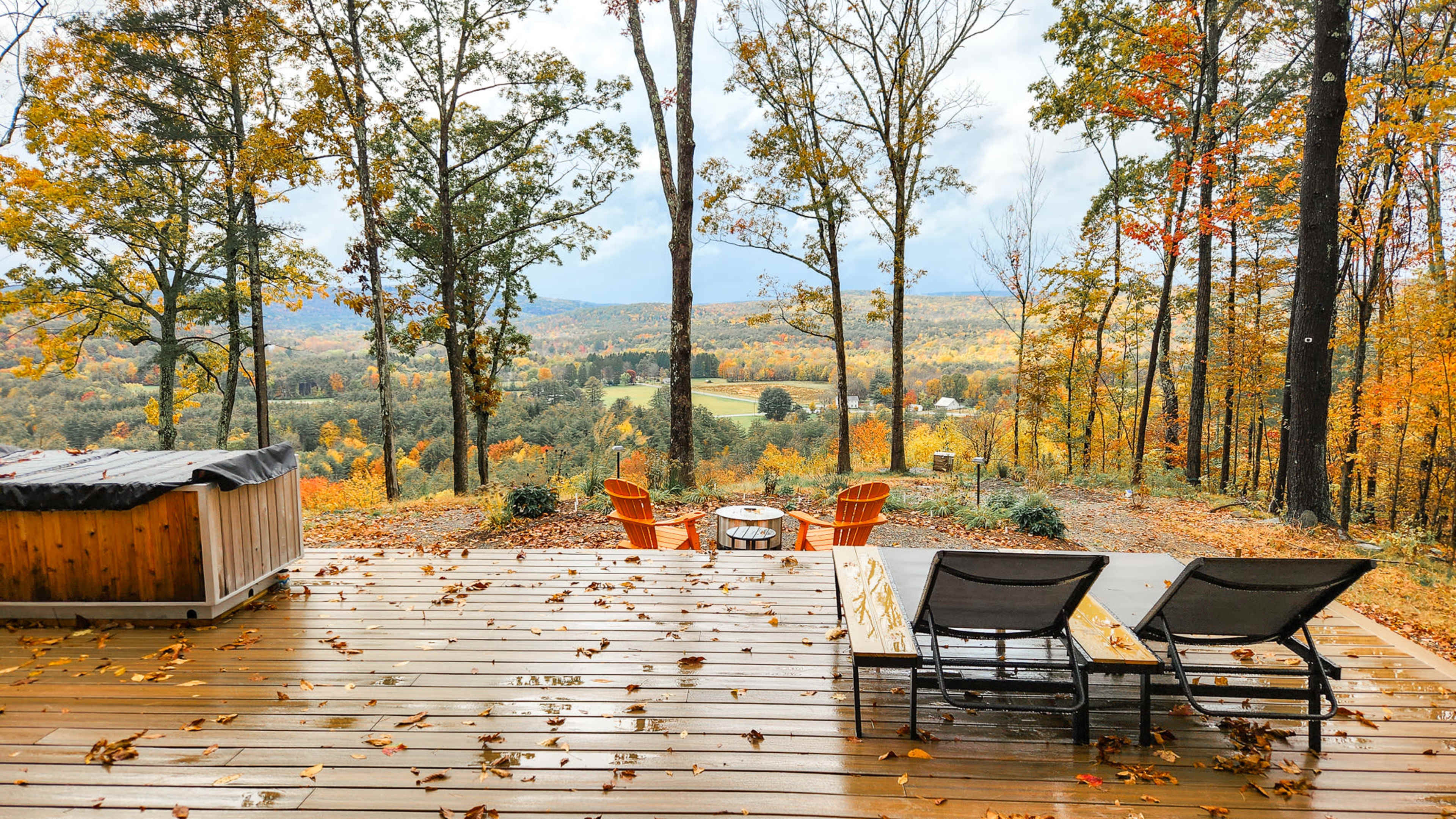The image shows a deck with two lounge chairs and a small table overlooking a colorful autumn landscape filled with trees and rolling hills.