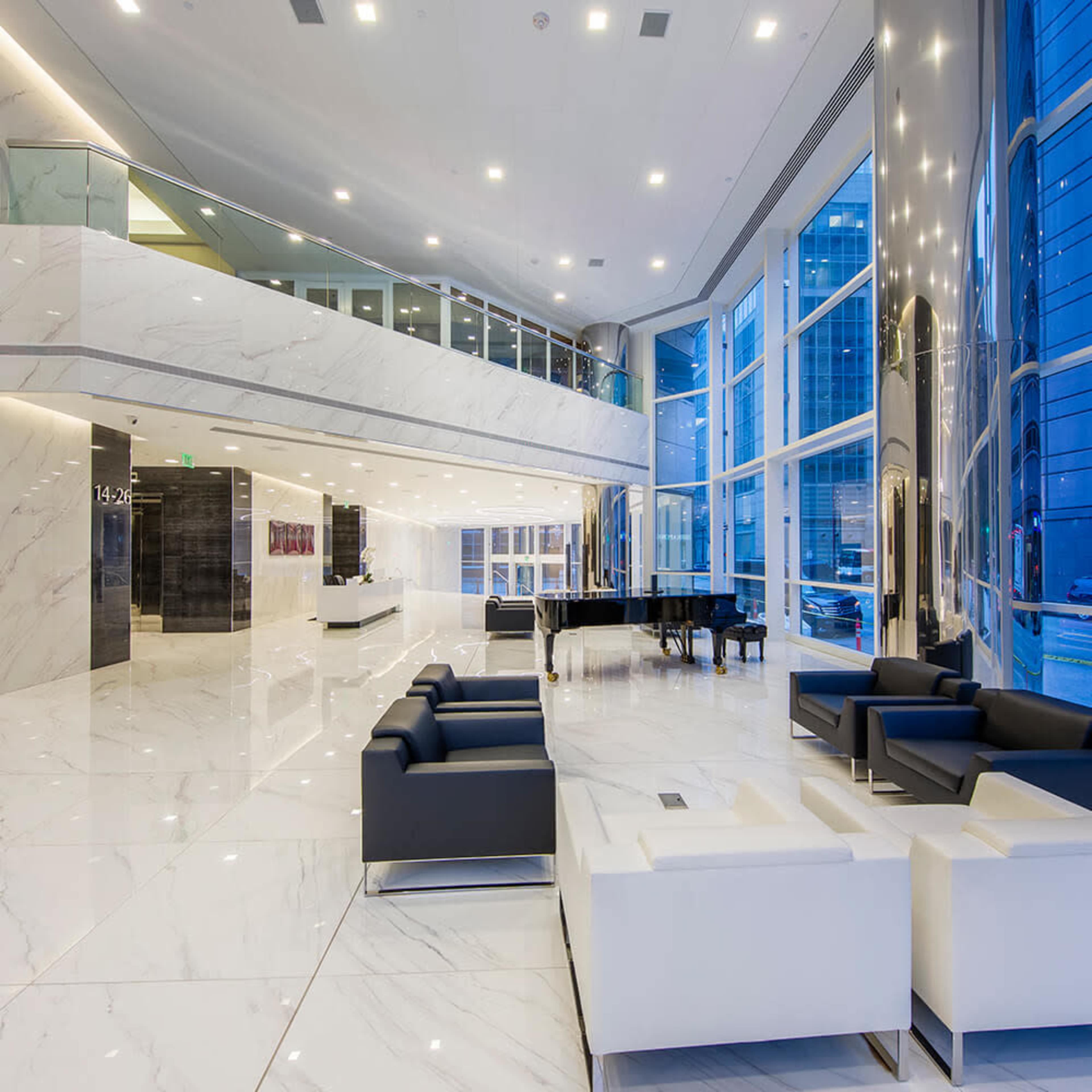 A spacious, modern lobby with marble floors, large windows, and contemporary furniture, including a grand piano.