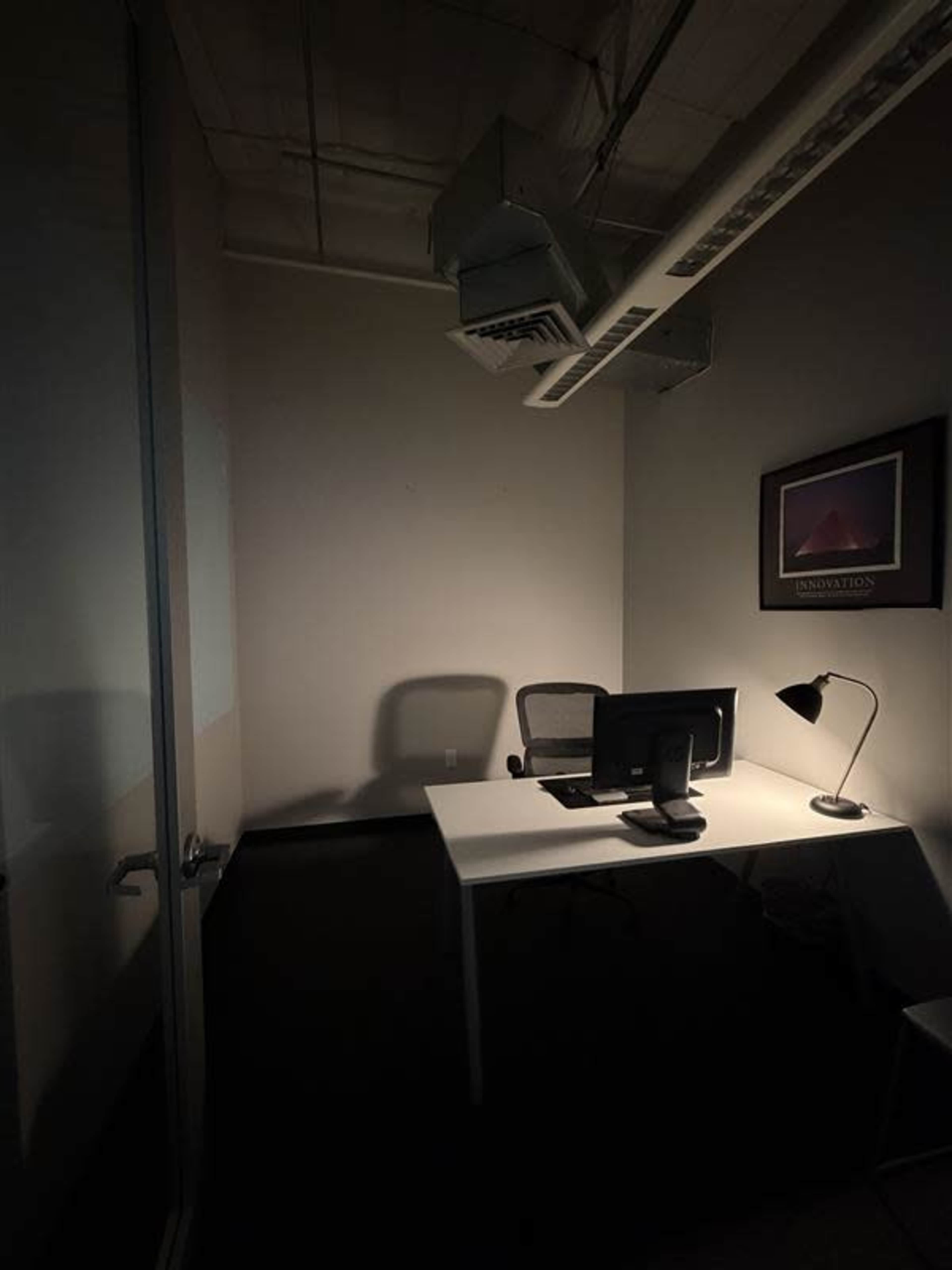 The image depicts a dimly lit office space featuring a desk with a computer monitor and a desk lamp.