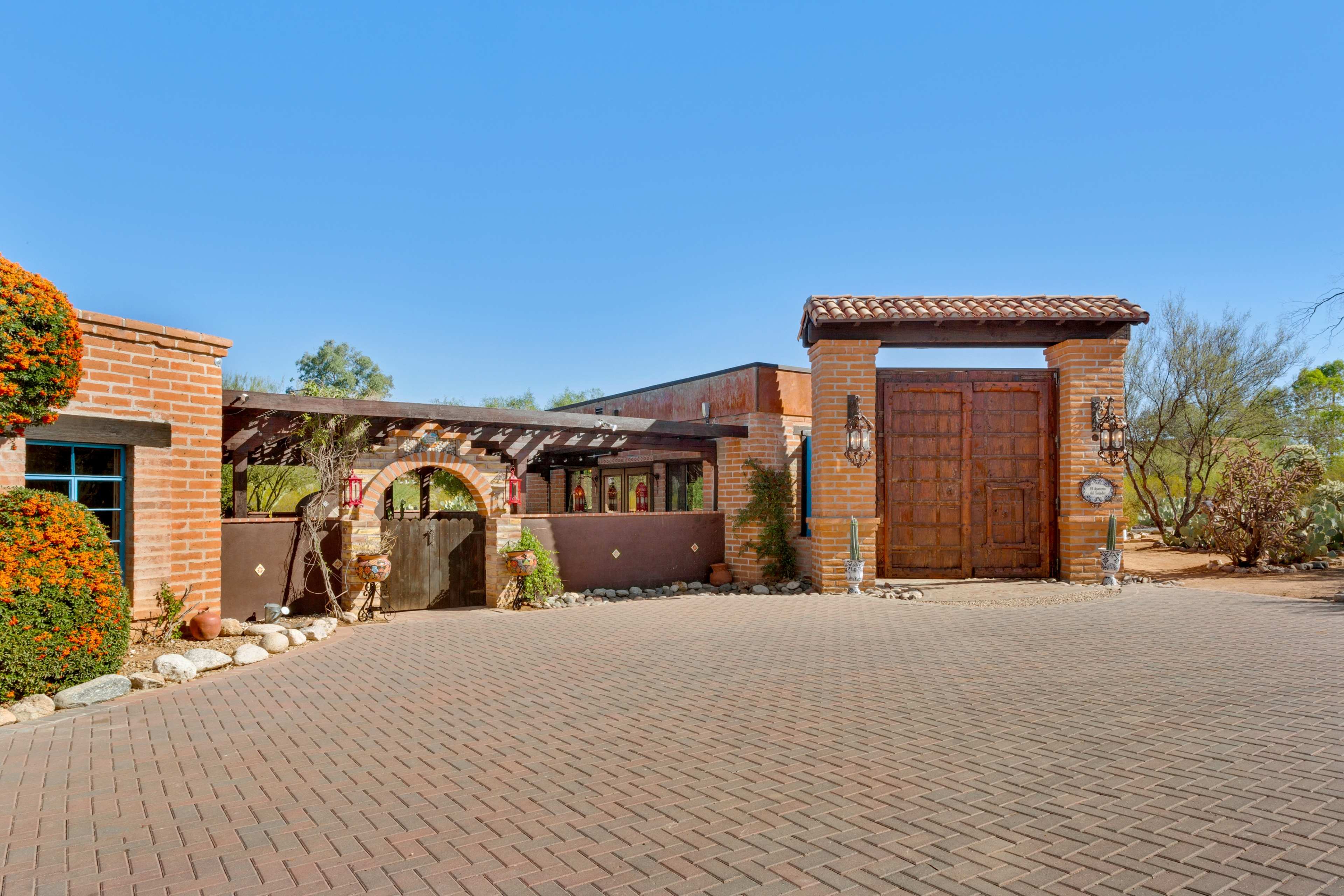 The scene features a southwestern-style house with a large wooden gate and landscaped gardens.