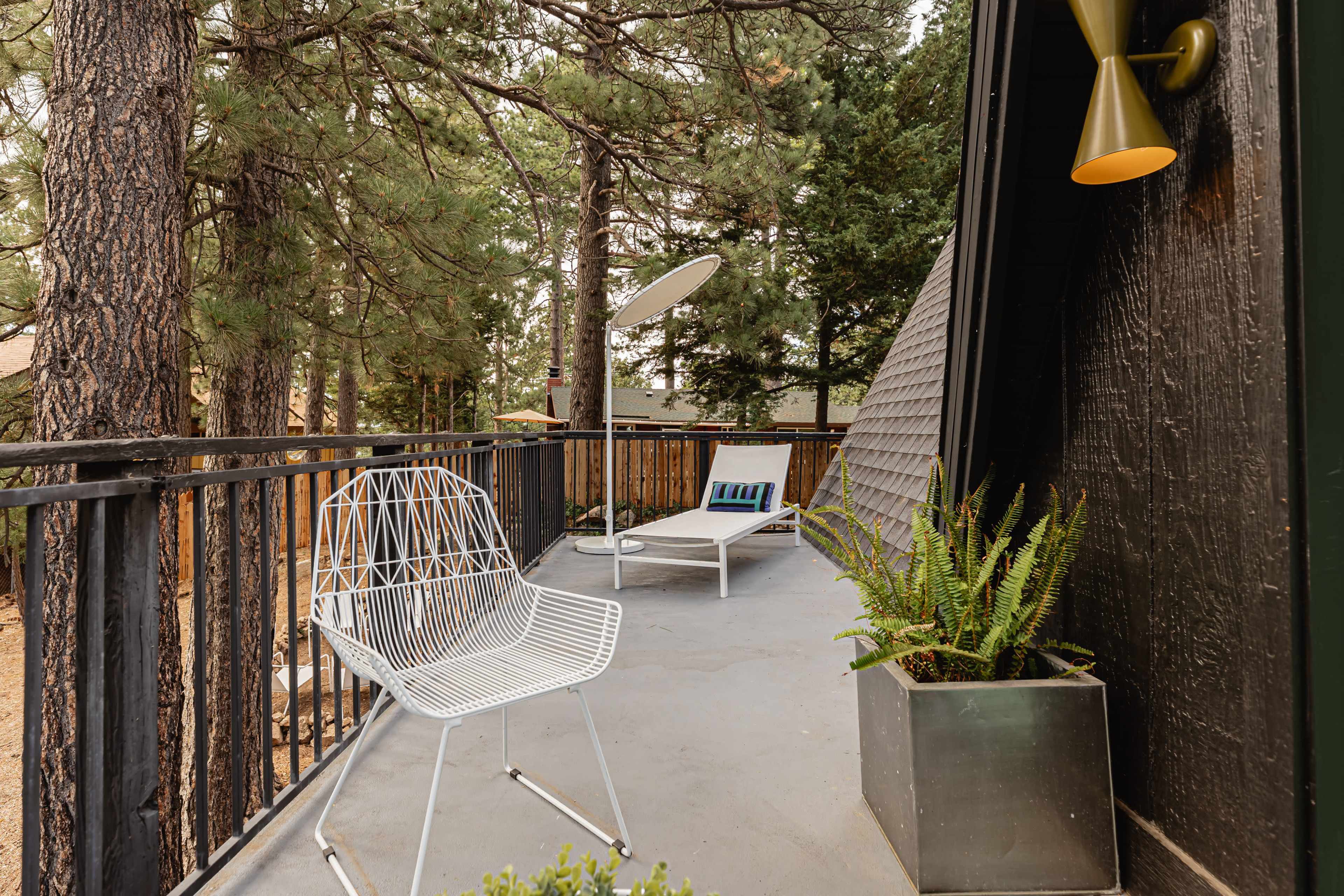 The image shows a balcony with two chairs, a small table, and potted plants, surrounded by trees and featuring a satellite dish.