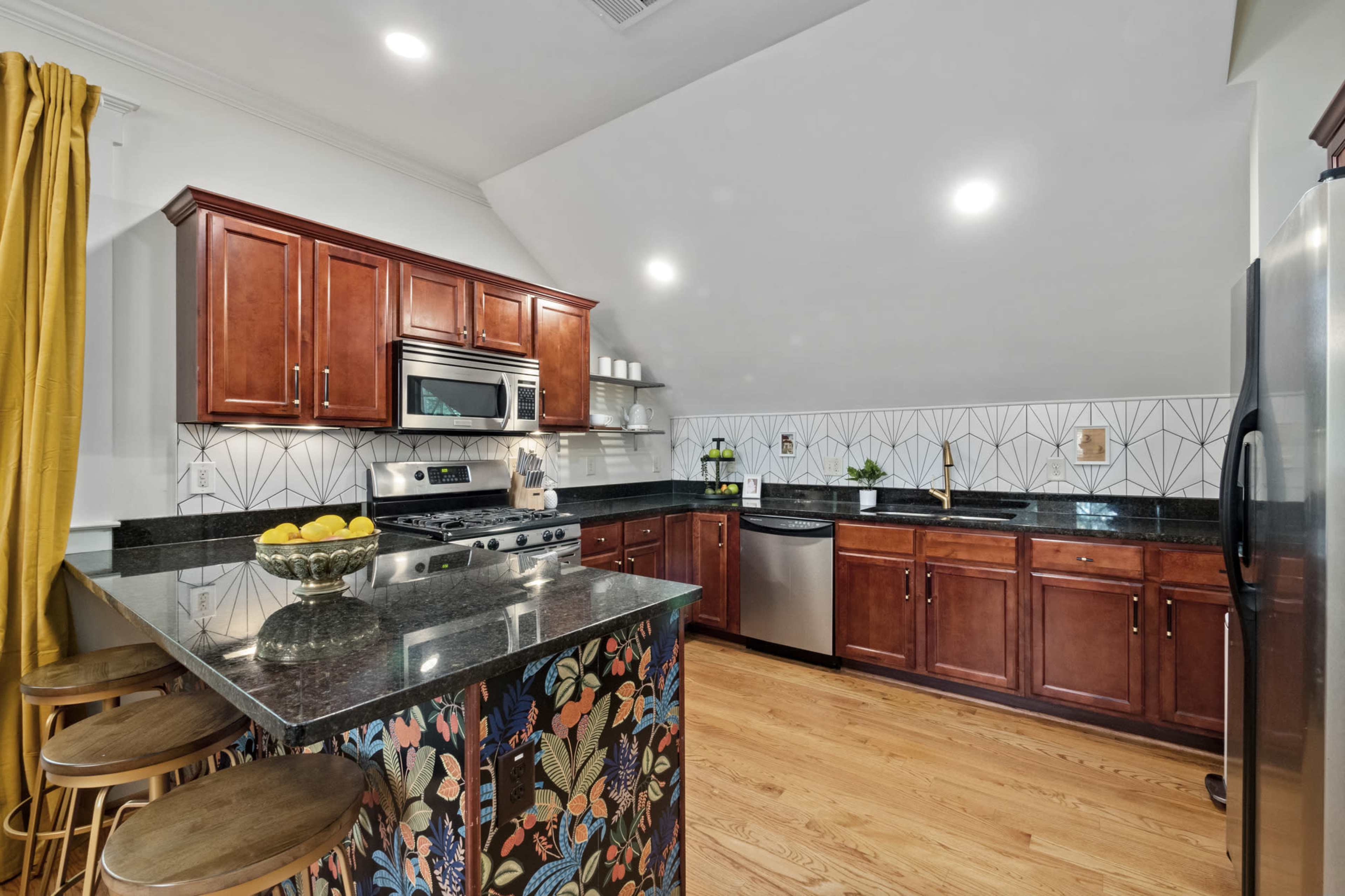 A modern kitchen with dark wood cabinetry, a black granite countertop, and a patterned backsplash featuring geometric designs.