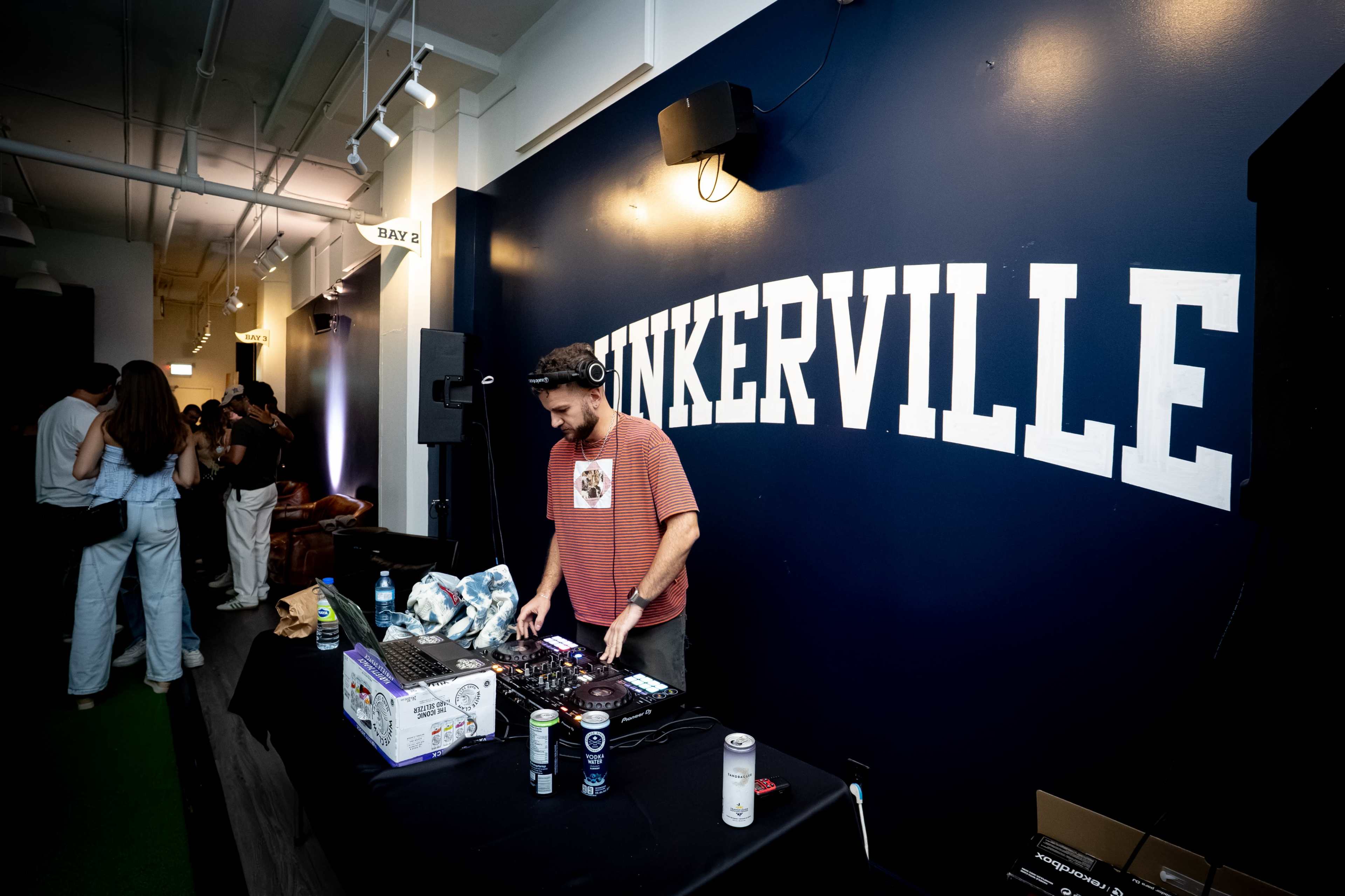 A DJ performs at a venue with the word "PUNKERVILLE" displayed prominently on the wall behind him.