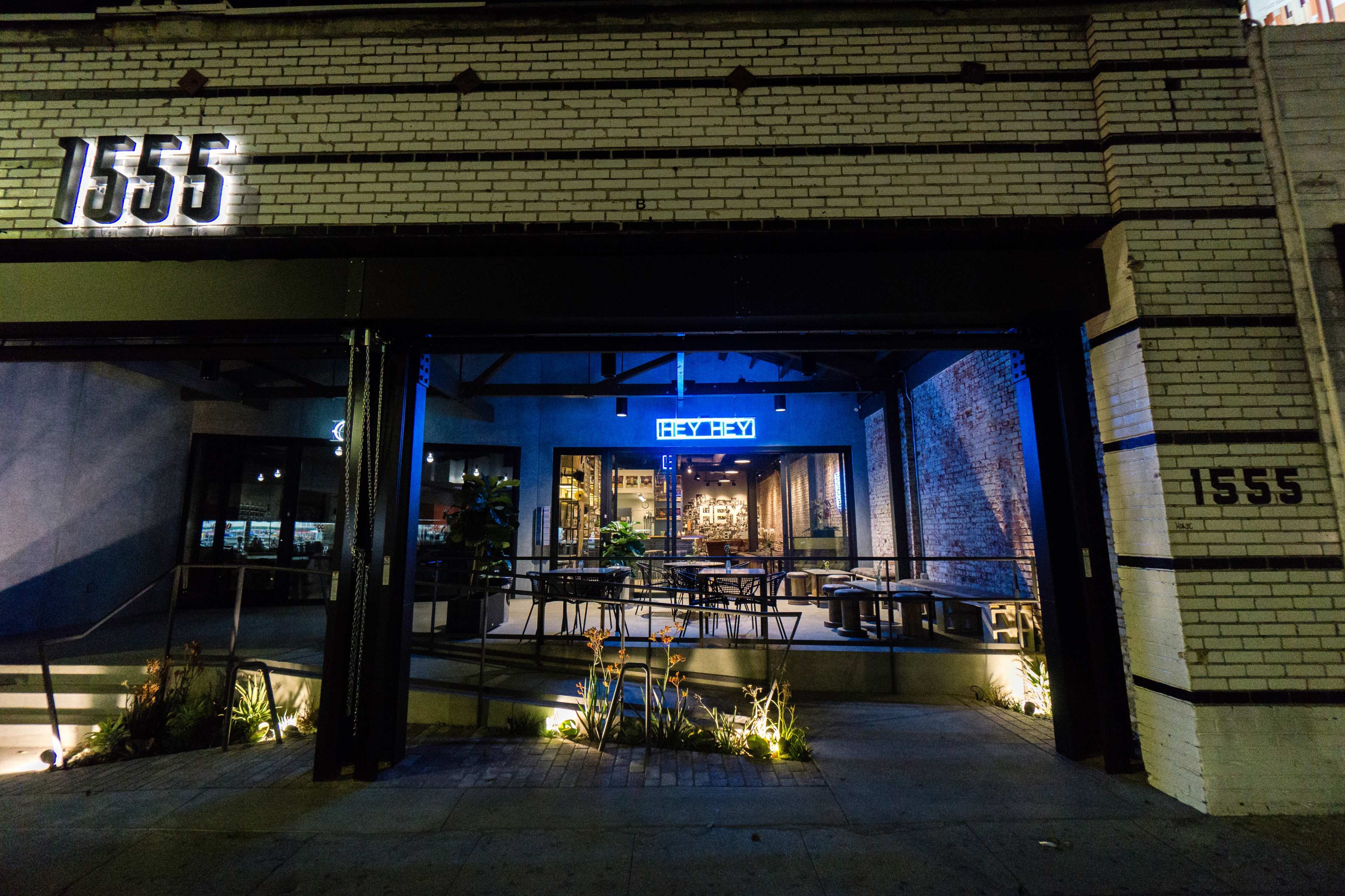 The exterior of a restaurant with a brightly lit facade, featuring large glass windows and seating available on the patio.