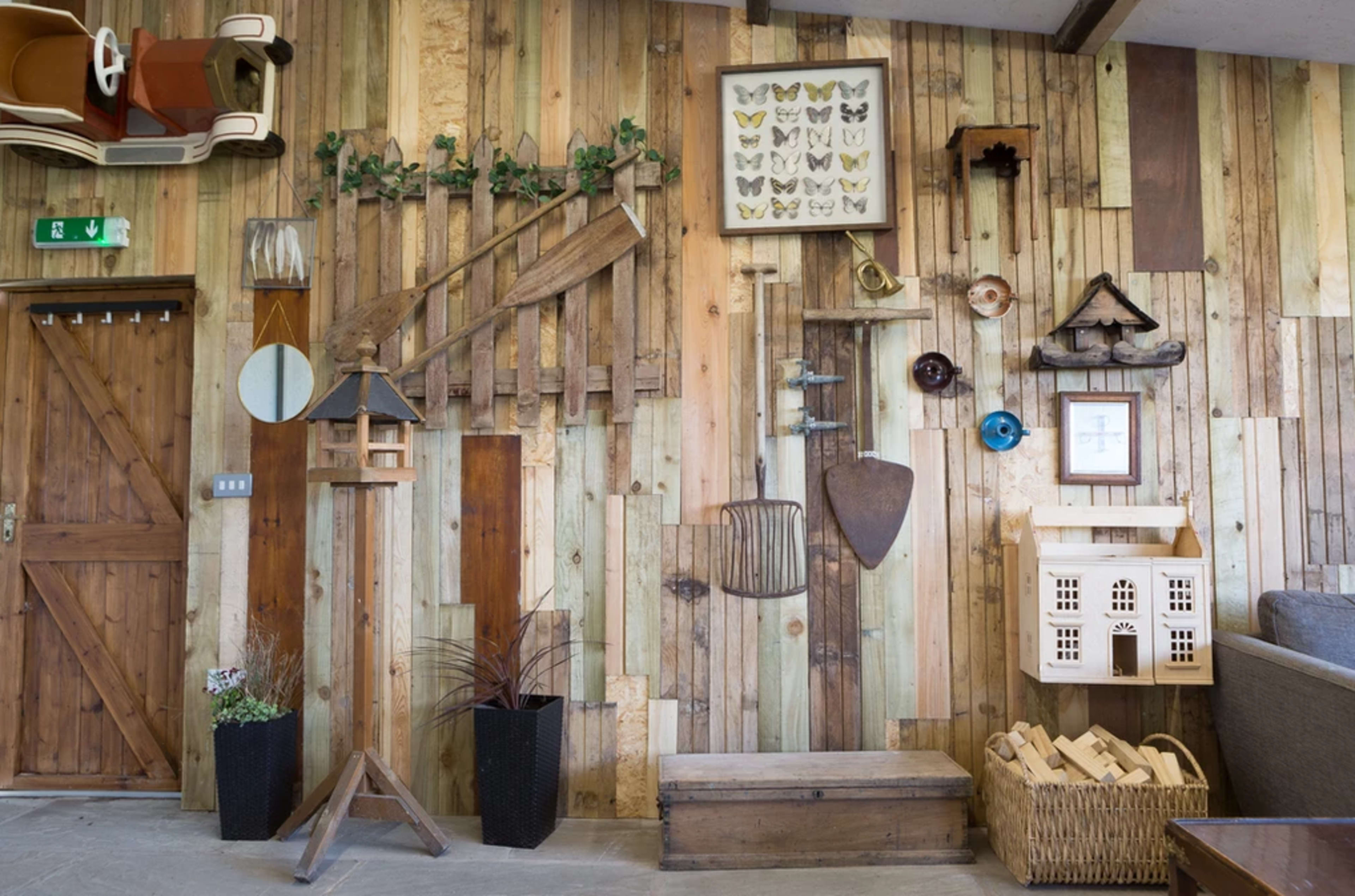 A wooden wall decorated with various items, including mirrors, artwork, birdhouses, and tools, complemented by plants and a door.
