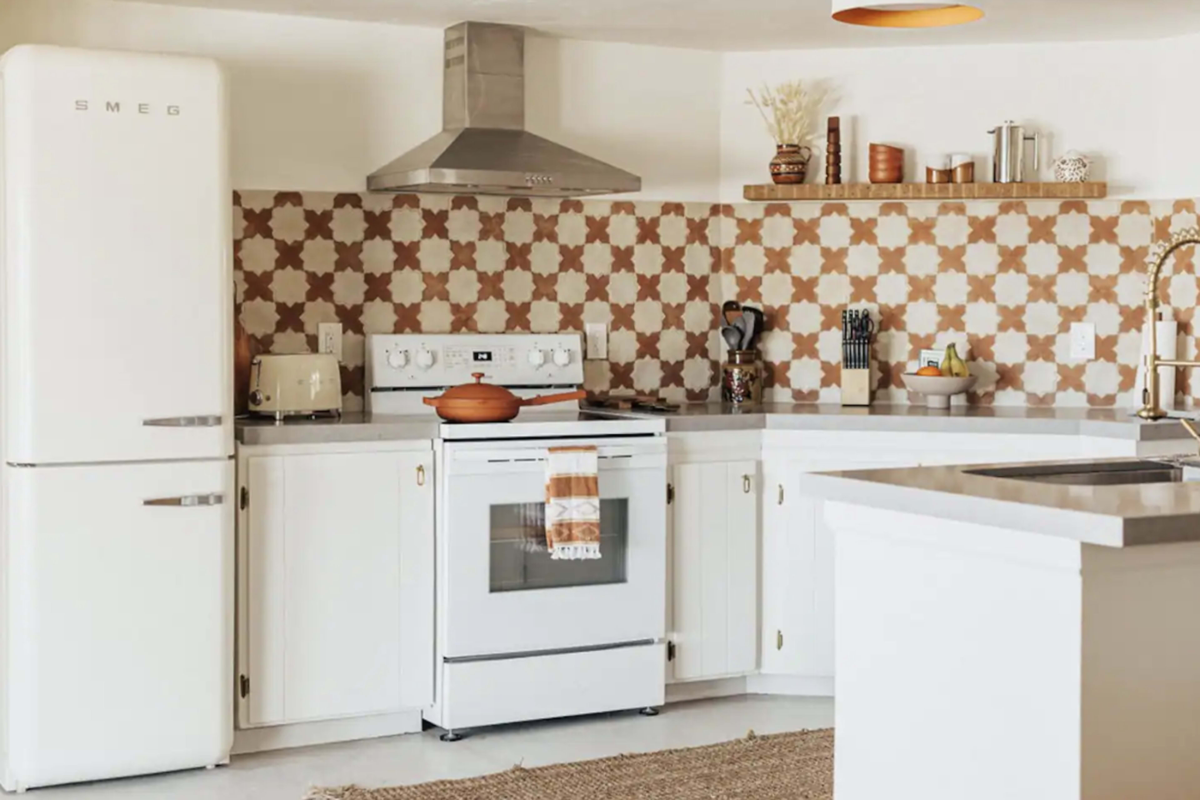 A modern kitchen features a white stove and refrigerator, decorative tiled backsplash, and a sink with various kitchen utensils.