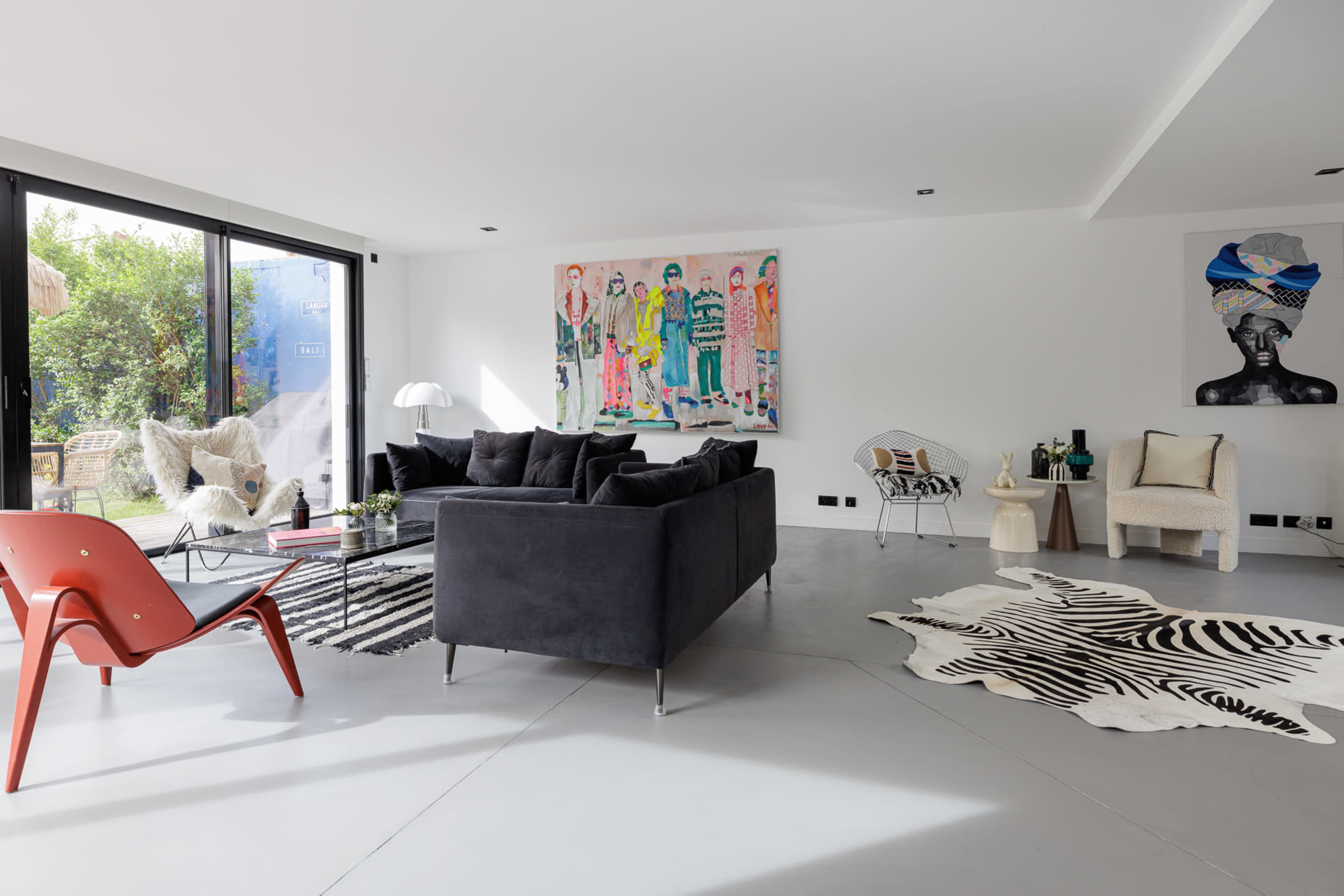 A modern living room featuring a dark couch, colorful artwork on the wall, and a mix of furniture including a red chair and a striped rug.
