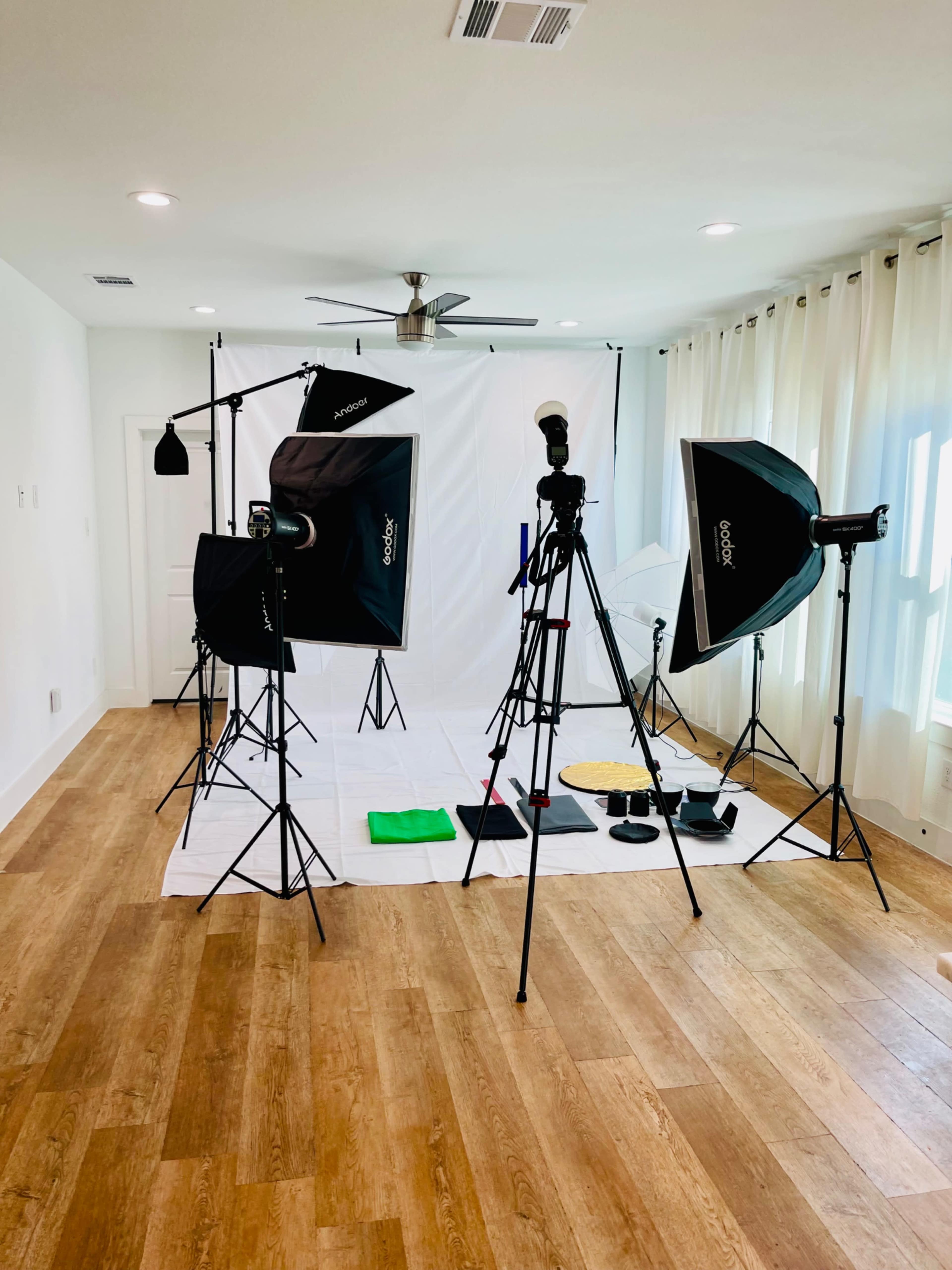 A photography studio setup with various lighting equipment, tripods, and a white backdrop on a wooden floor.