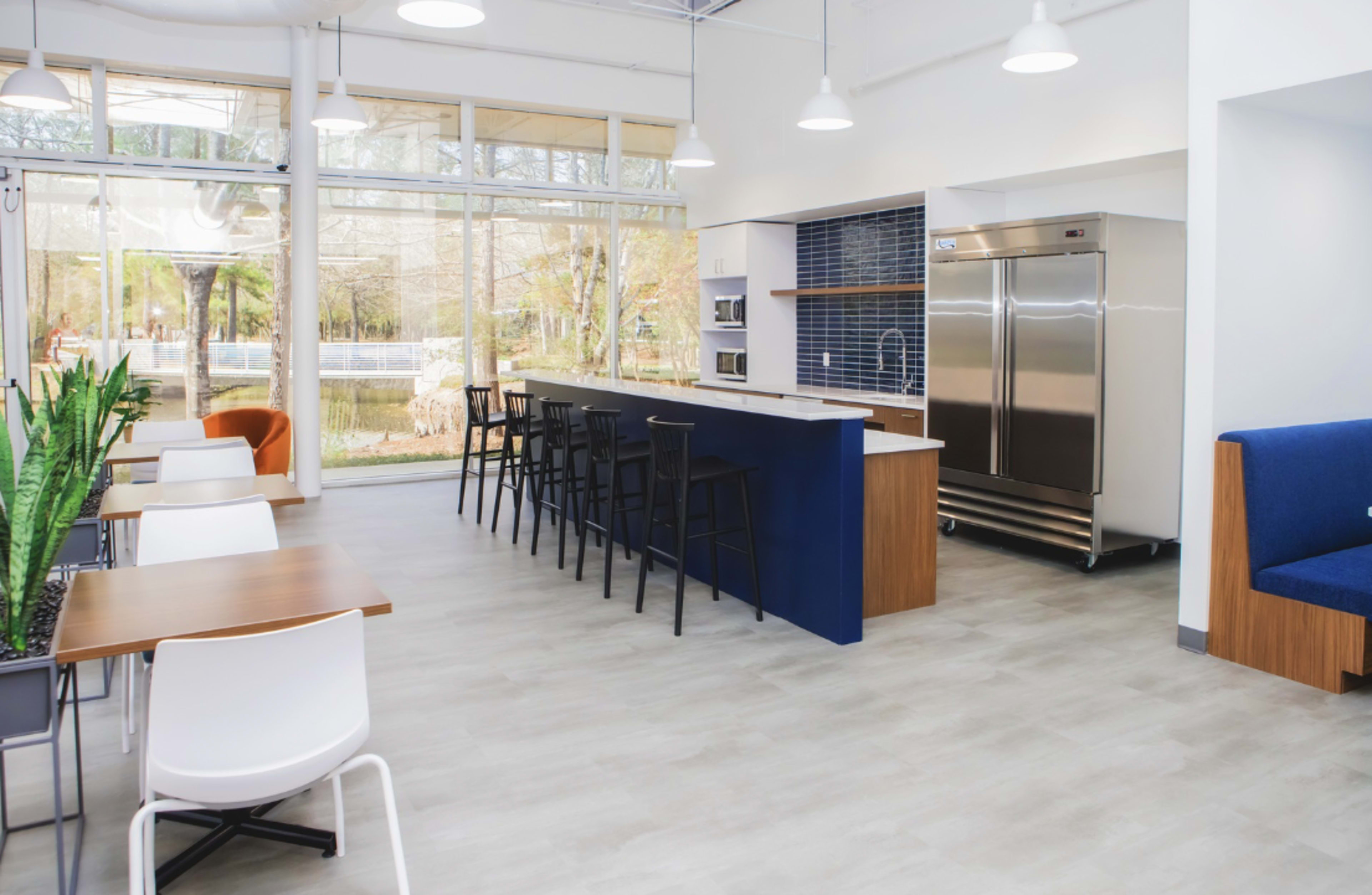 A modern kitchen and dining area with a long island counter, bar stools, stainless steel refrigerator, and large windows overlooking a scenic view.