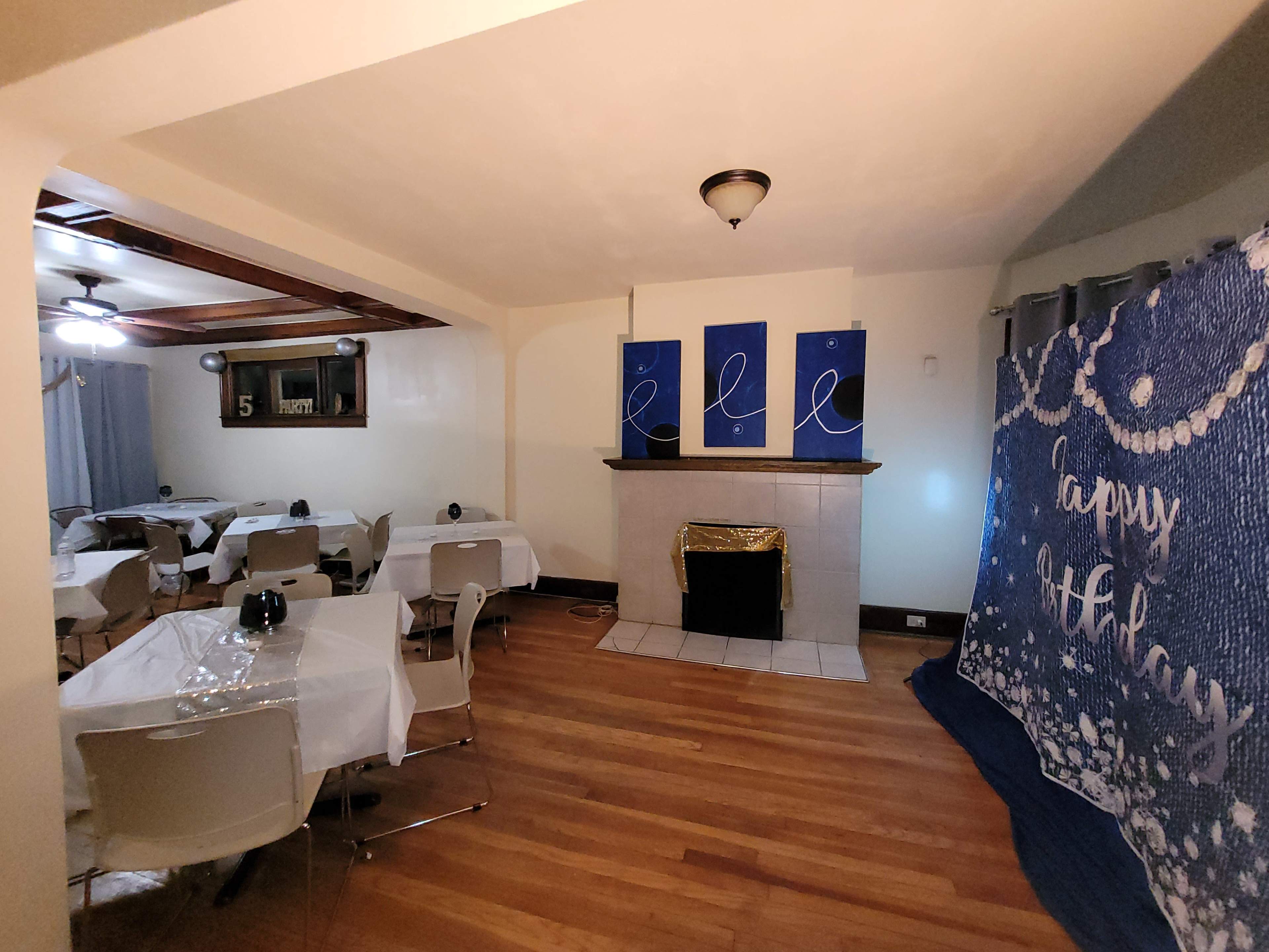 A decorated room with tables covered in white tablecloths, a fireplace with gold trim, and a blue birthday backdrop on the wall.