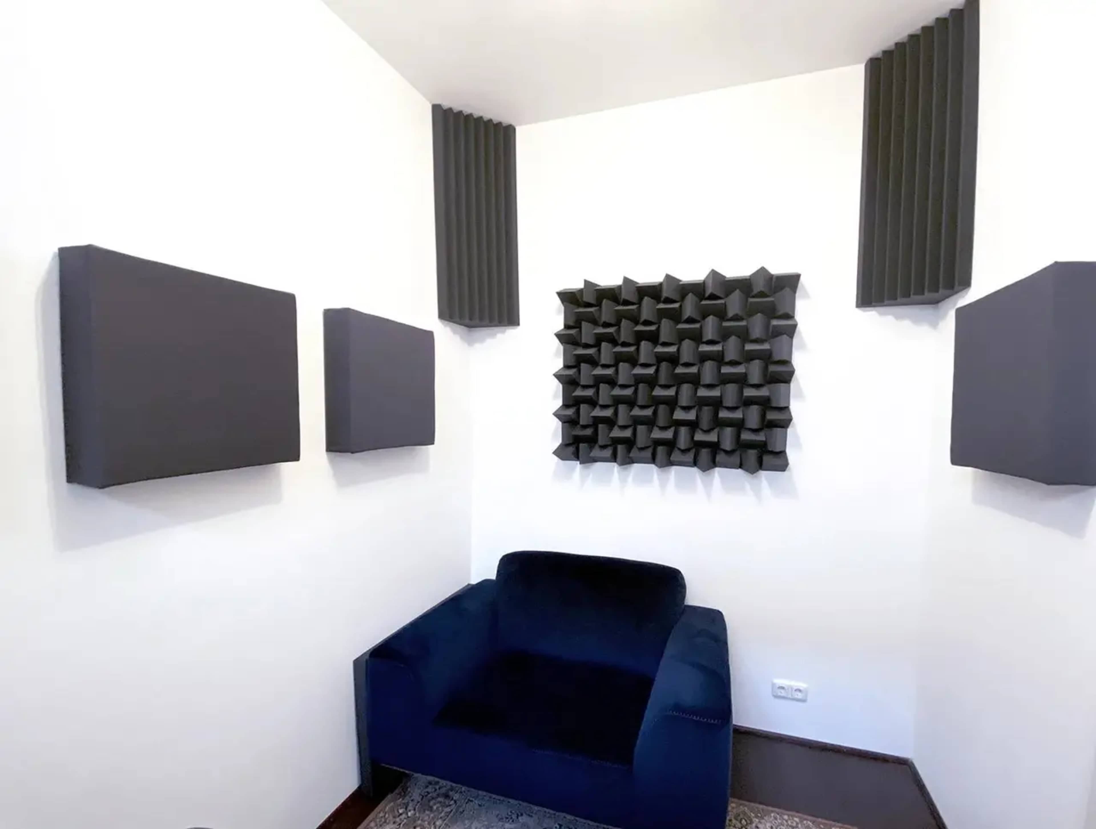 A soundproofed room with black acoustic panels on the walls and a blue armchair in the corner.