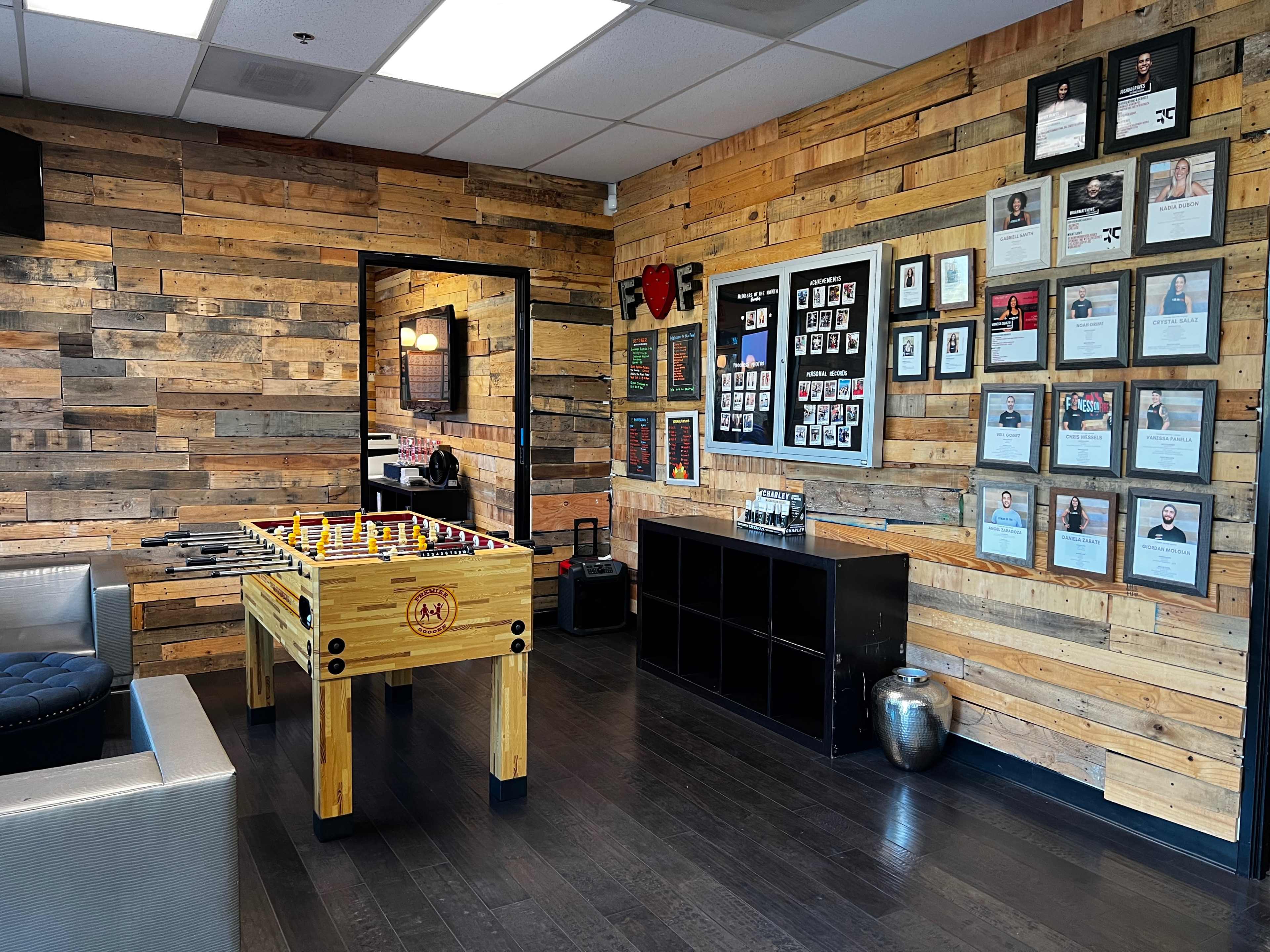 A room with a foosball table, wooden pallet walls, and framed certificates and photographs displayed on one wall.
