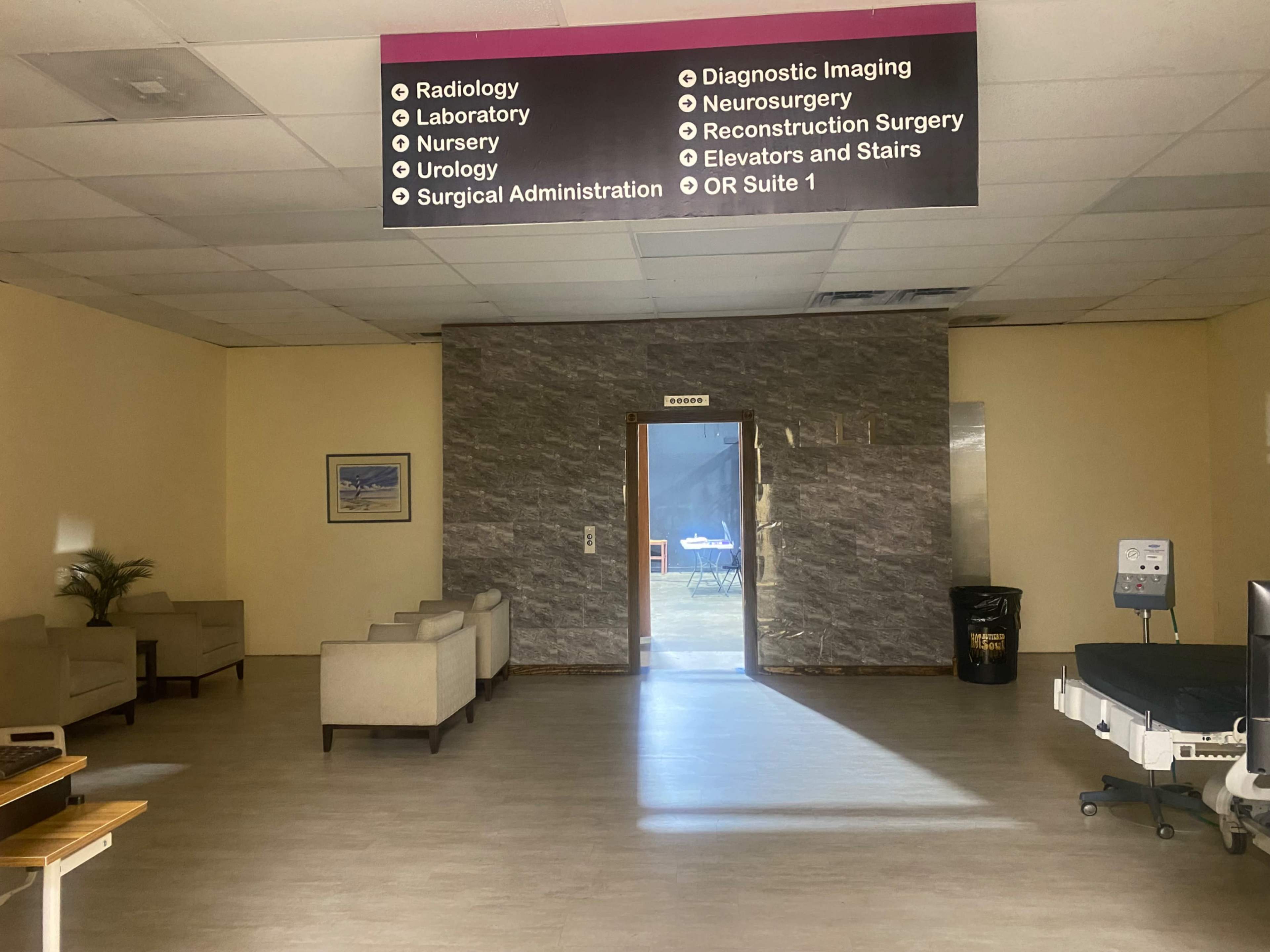 The image shows a hospital waiting area with seating and directional signage for various departments.
