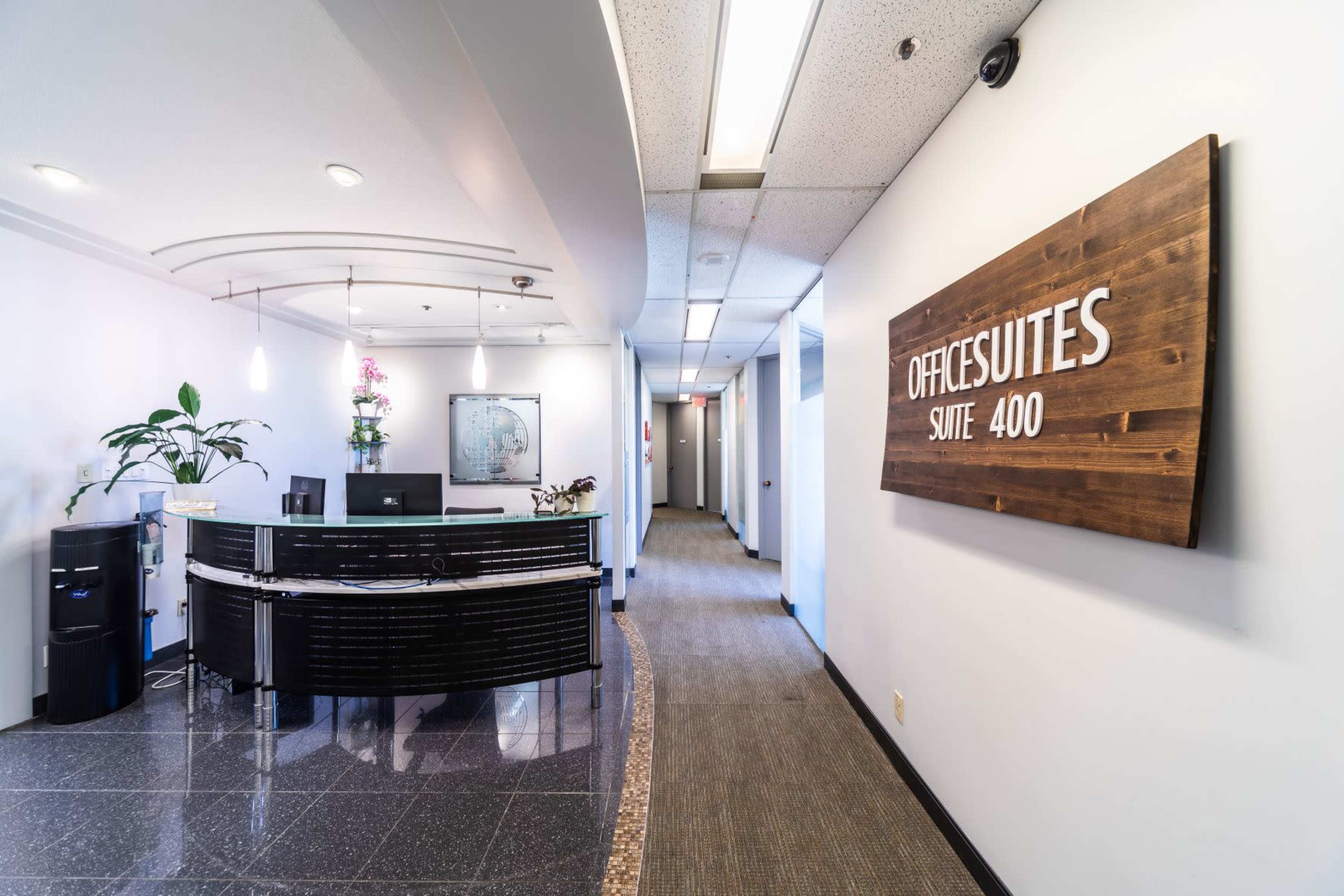A modern office reception area with a curved front desk and a sign indicating "OFFICESUITES SUITE 400" on the wall.