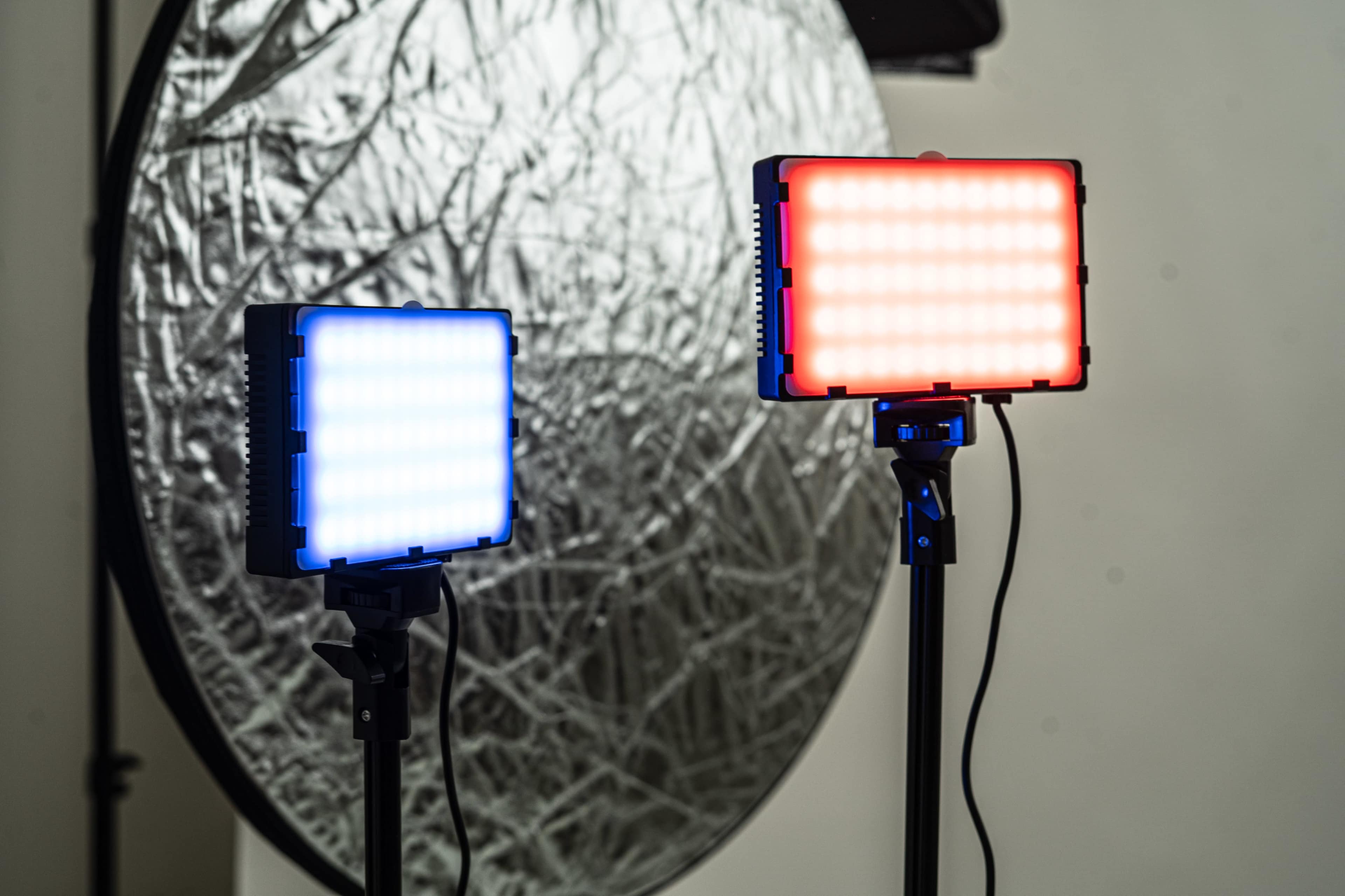 Two LED lights on stands, one emitting blue light and the other emitting red light, in front of a circular reflective surface.