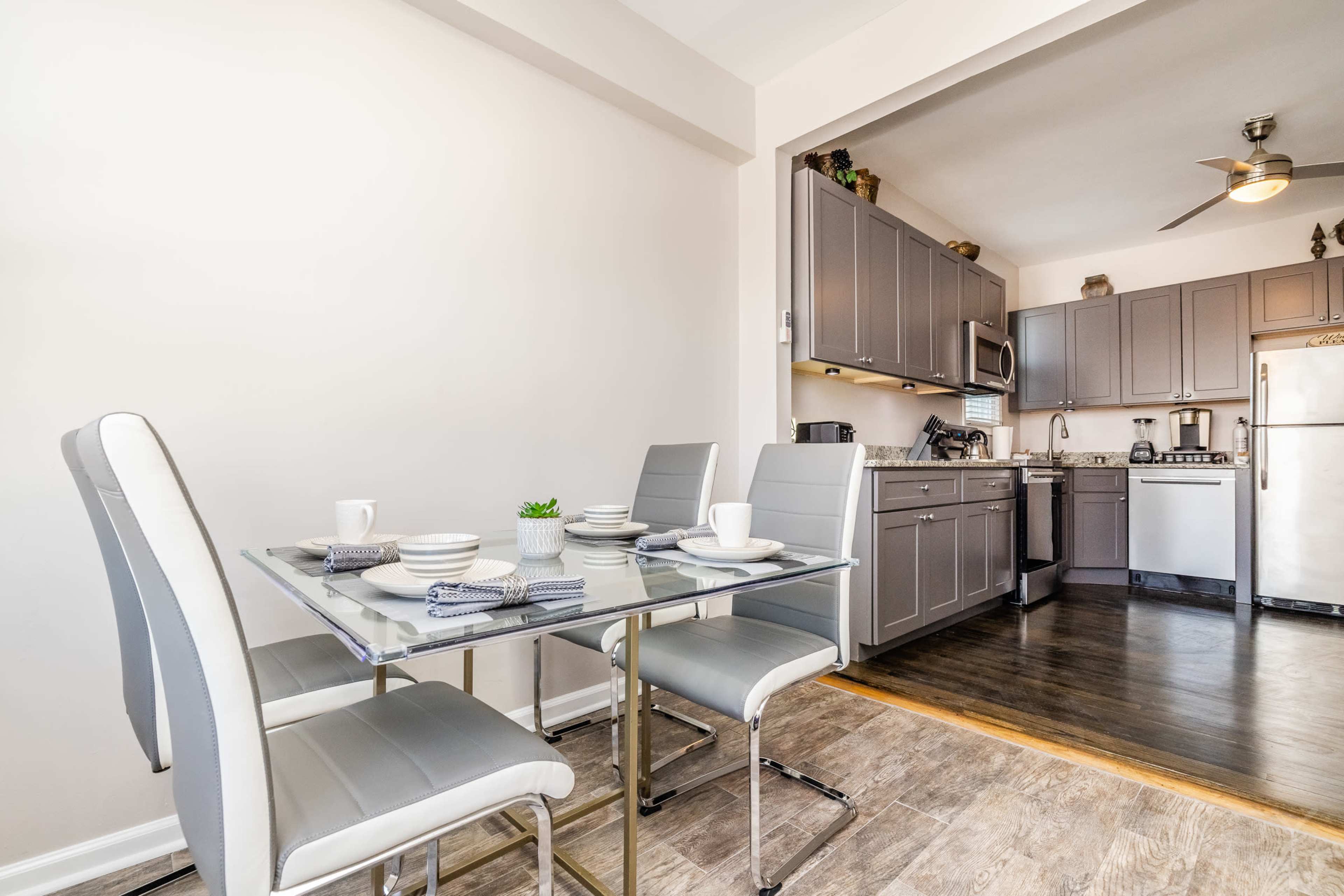 A modern kitchen features a dining table set for three, with gray chairs and a view of cabinetry and appliances in the background.