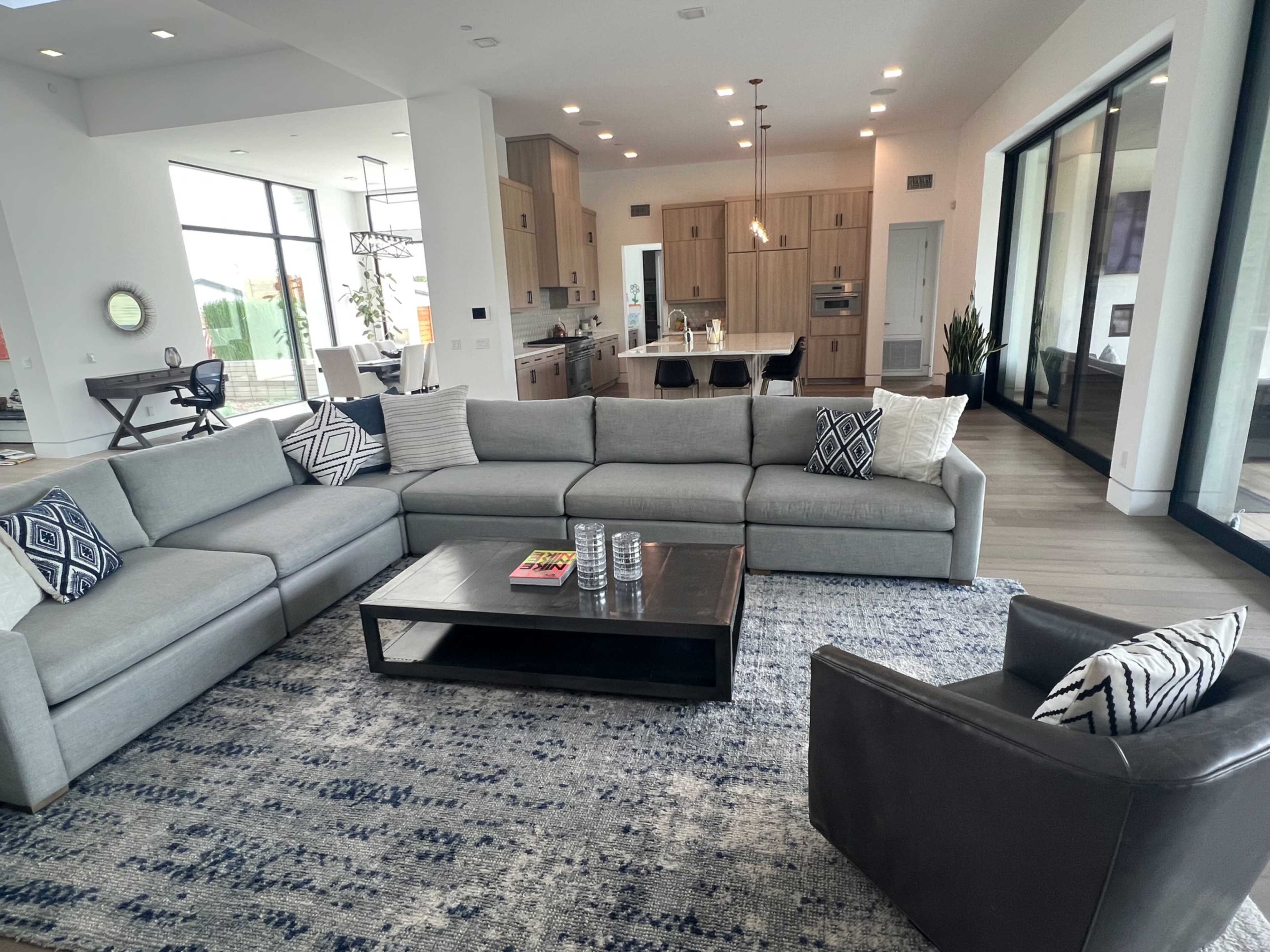 A modern living room with a sectional sofa, a coffee table, and a view of an open kitchen in the background.