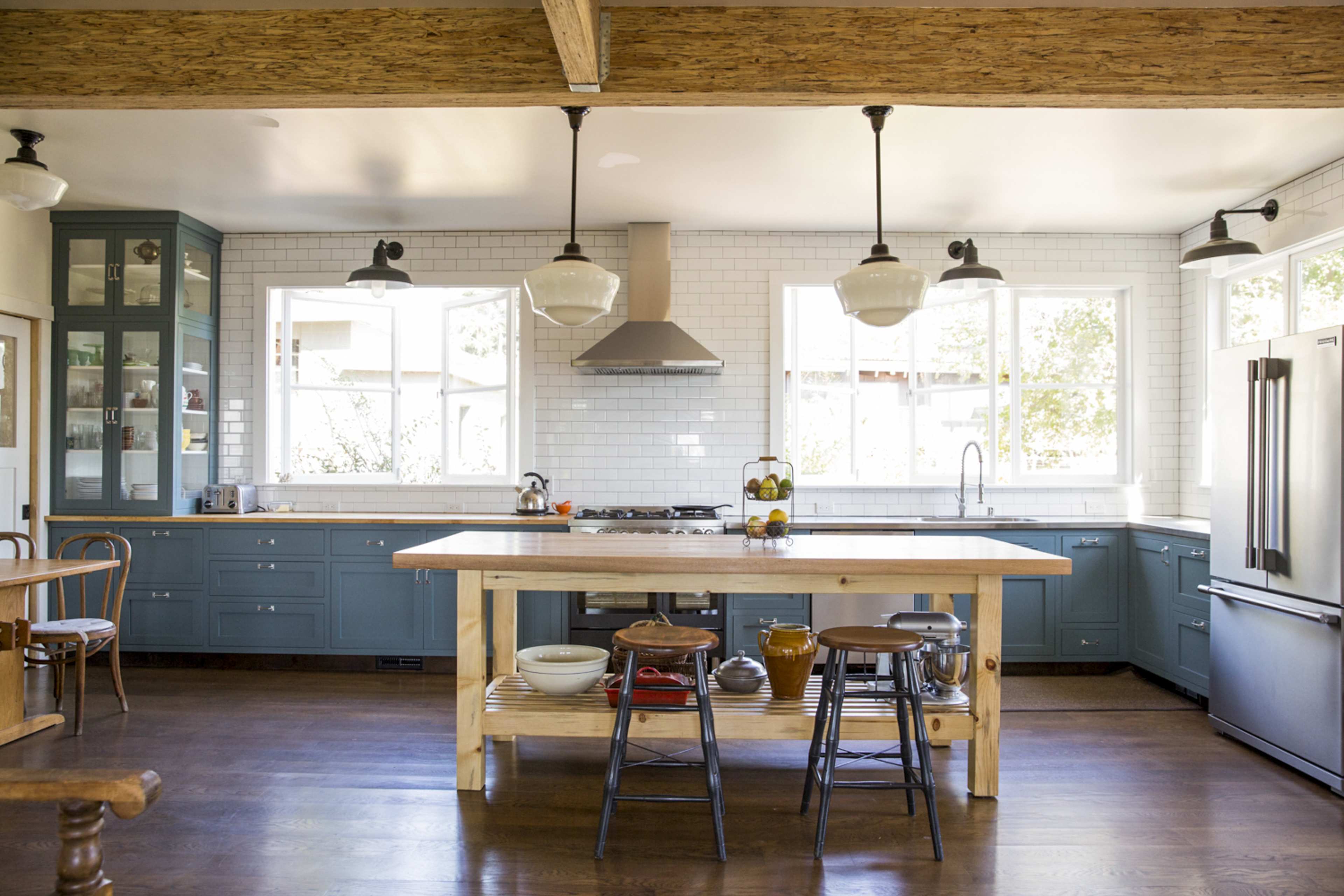The kitchen features blue cabinets, a large wooden island with stools, and large windows allowing natural light to fill the space.