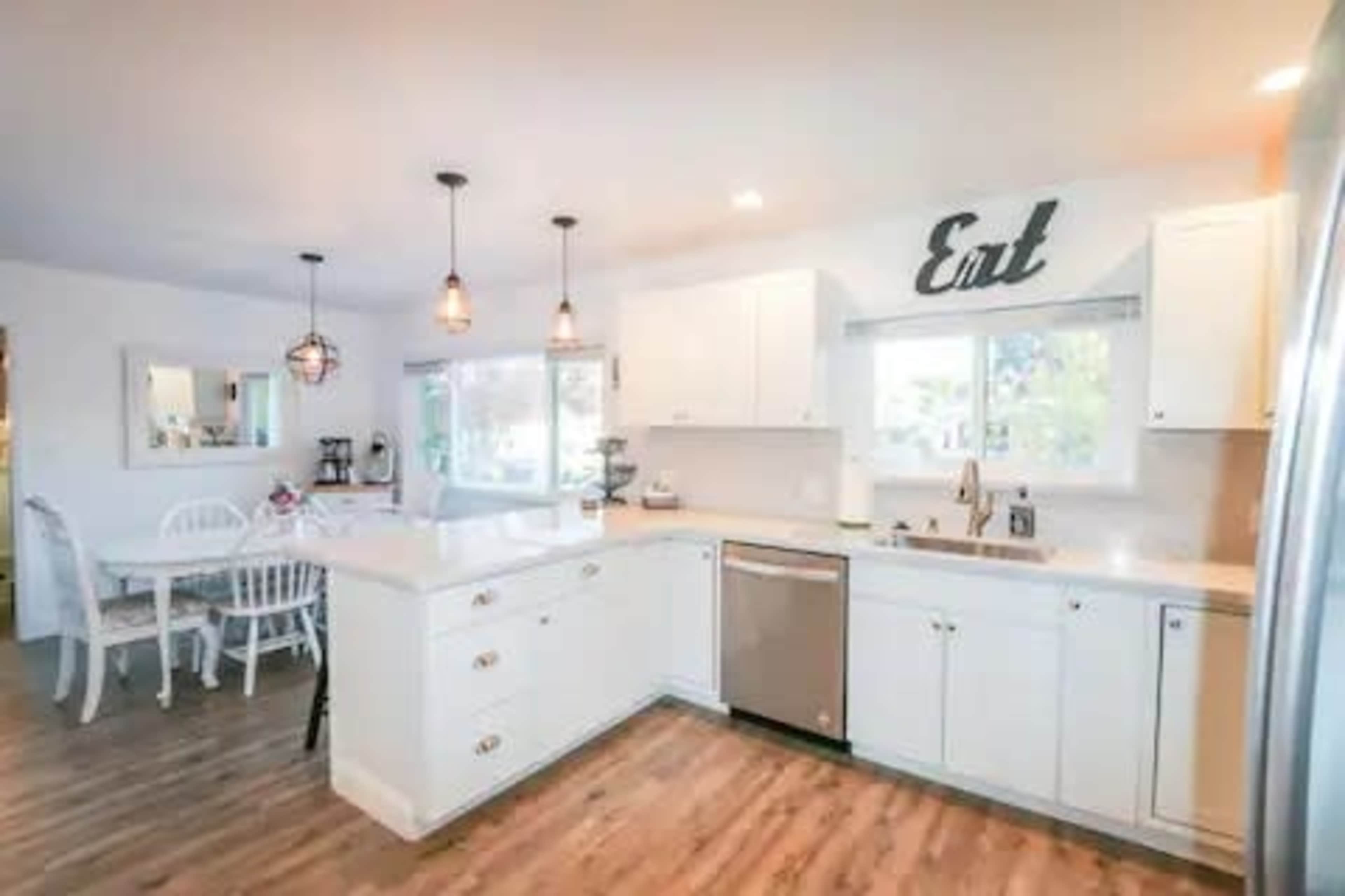 A modern kitchen features white cabinetry, stainless steel appliances, and a dining area with a white table and chairs.