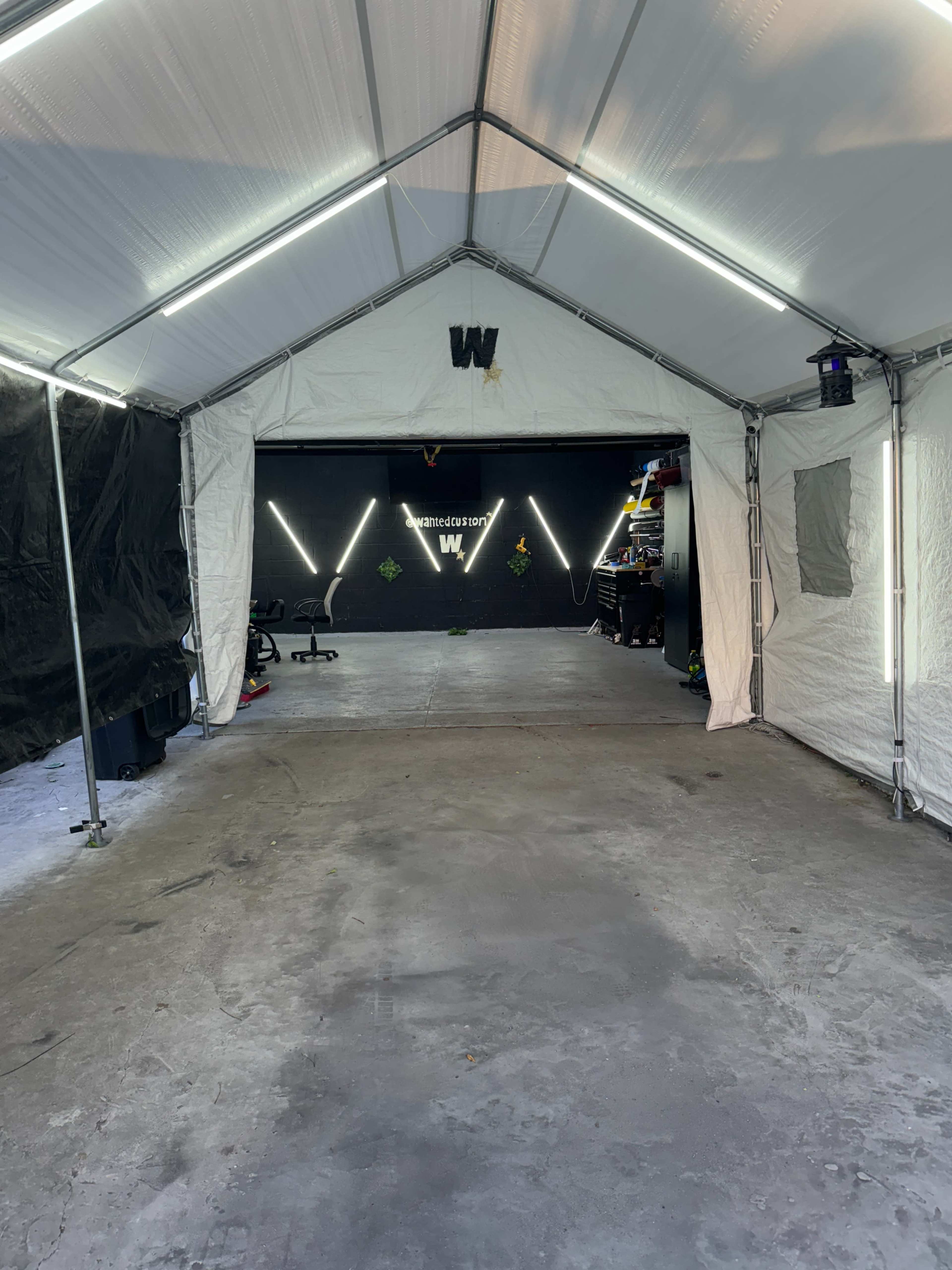 The interior of a tent with a concrete floor, leading to a dark space adorned with LED lights and a prominent logo on the wall.
