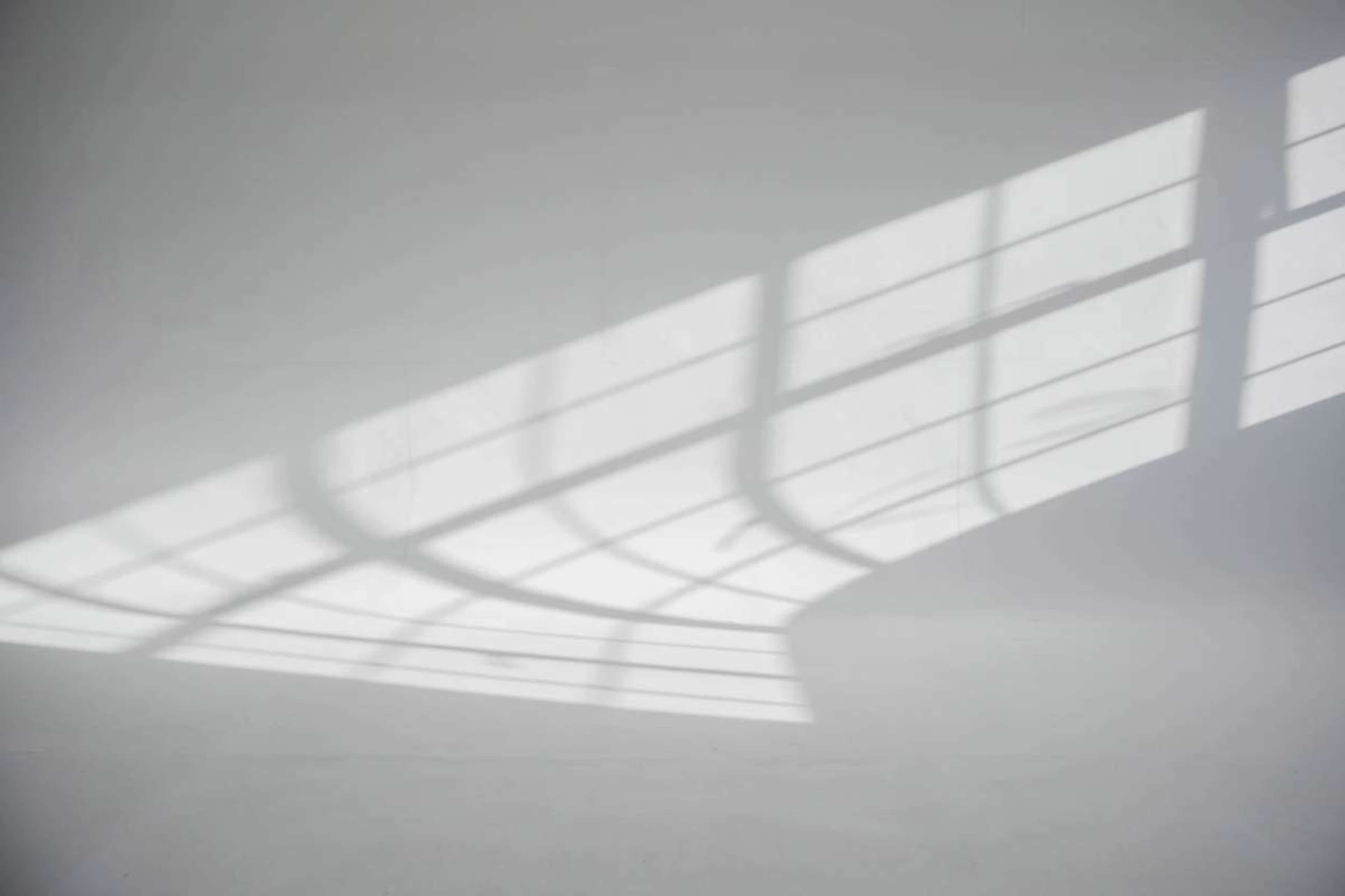The image shows a series of geometric shadows cast on a white surface by a window with a grid design.