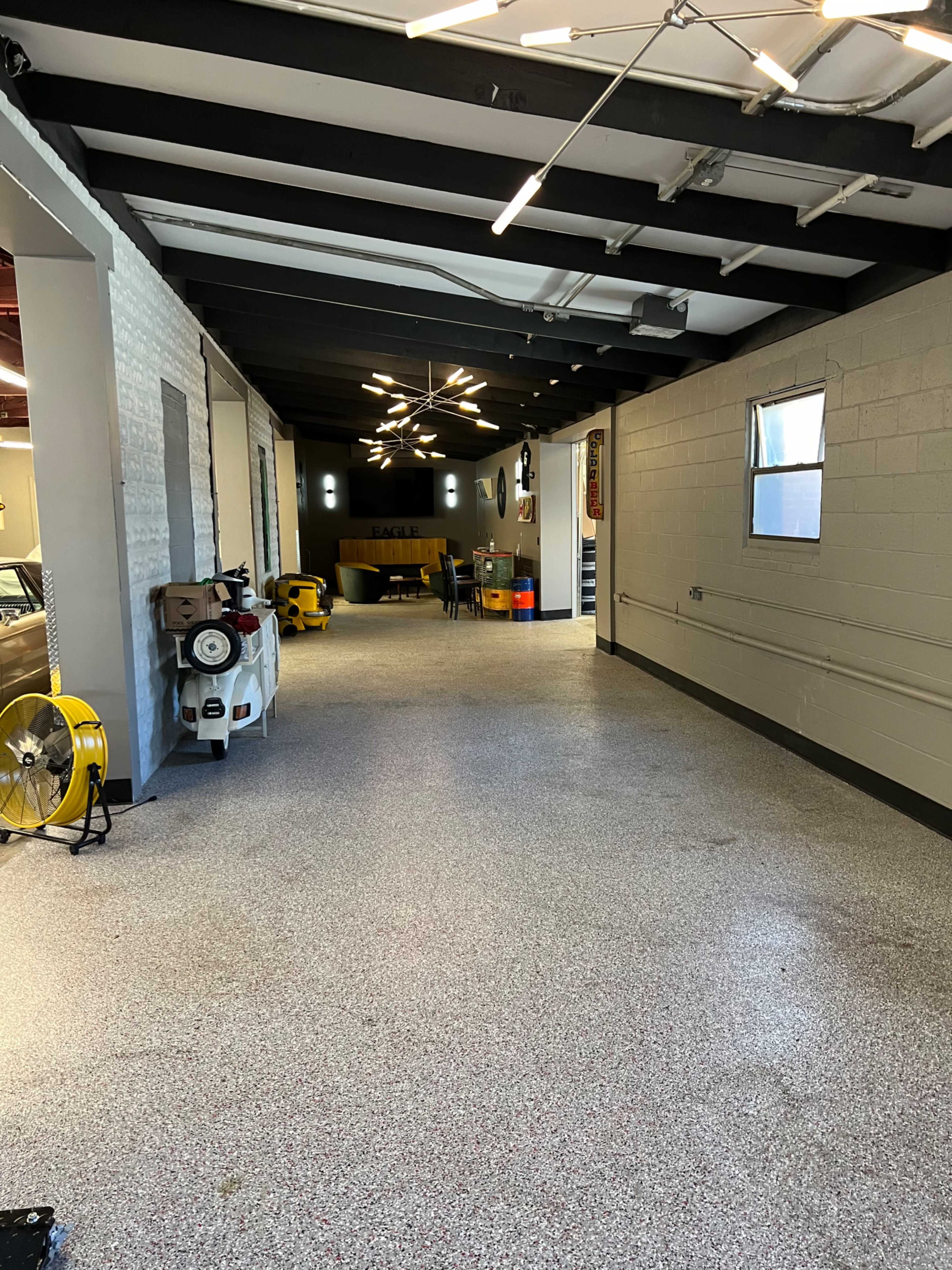 A spacious, well-lit corridor with a textured floor, flanked by painted walls and illuminated by modern light fixtures.