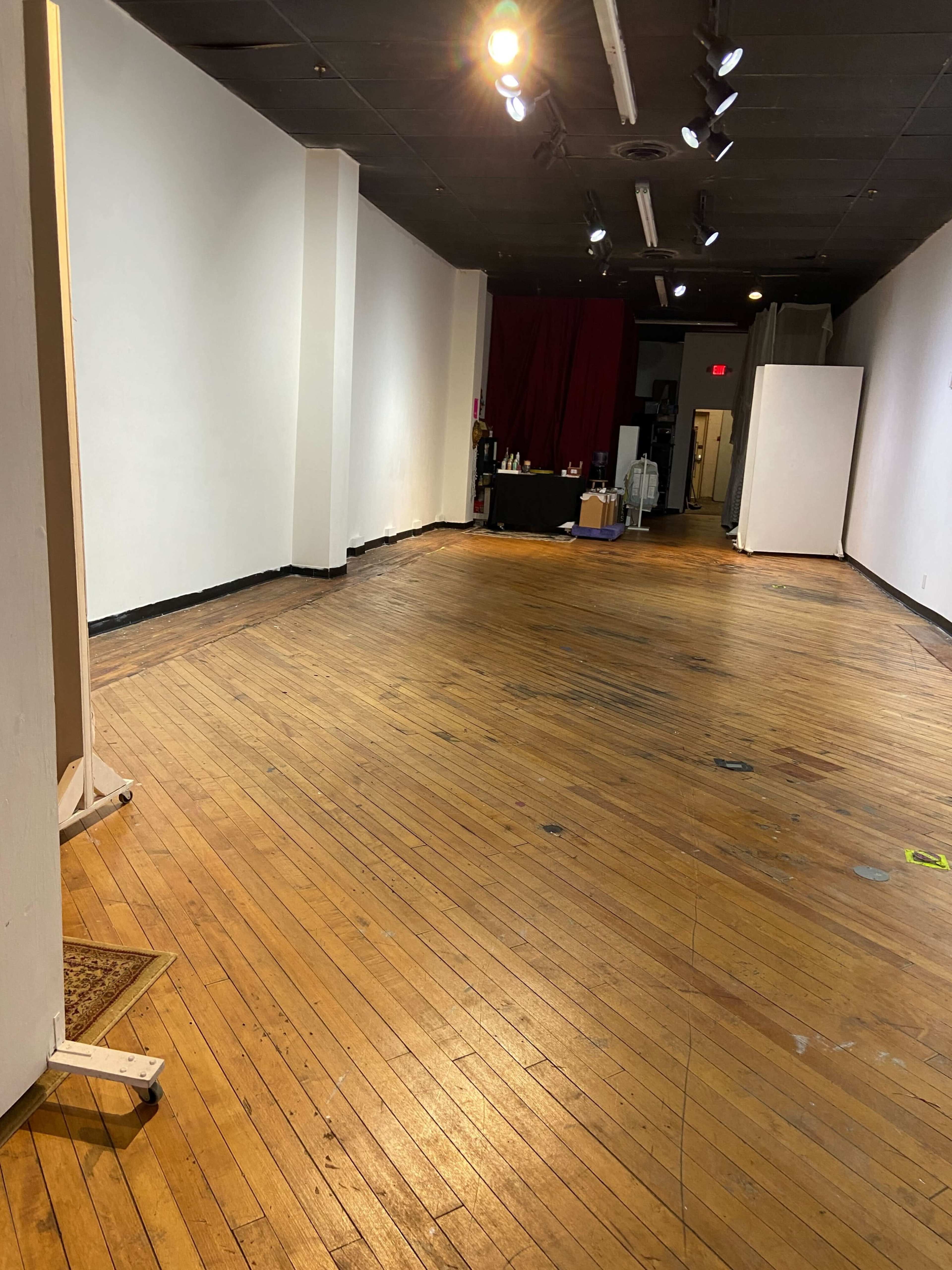 A spacious room with wooden floors, white walls, and minimal furniture at the far end.