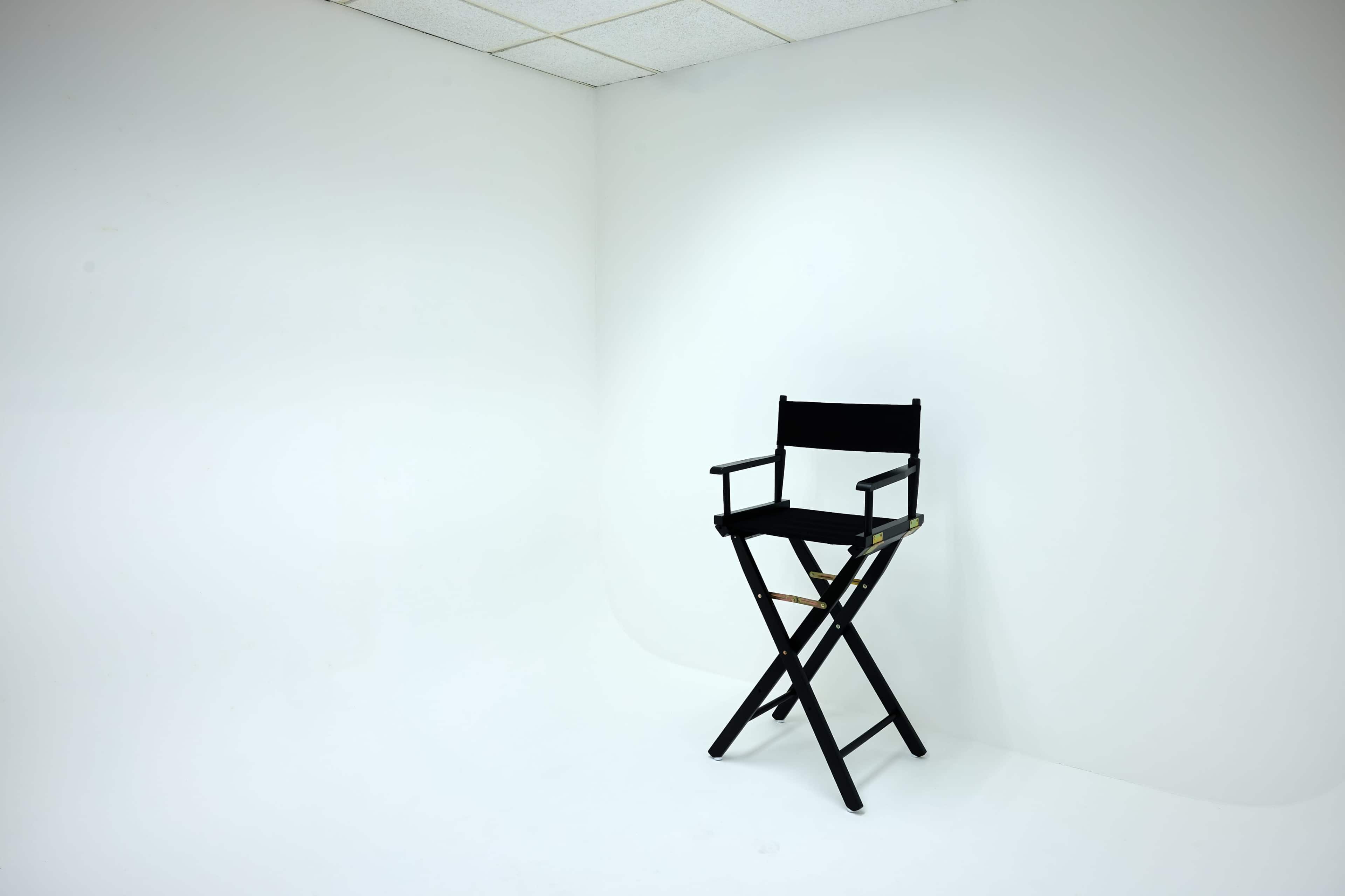 A black director's chair is positioned against a plain white wall in a sparsely furnished room.
