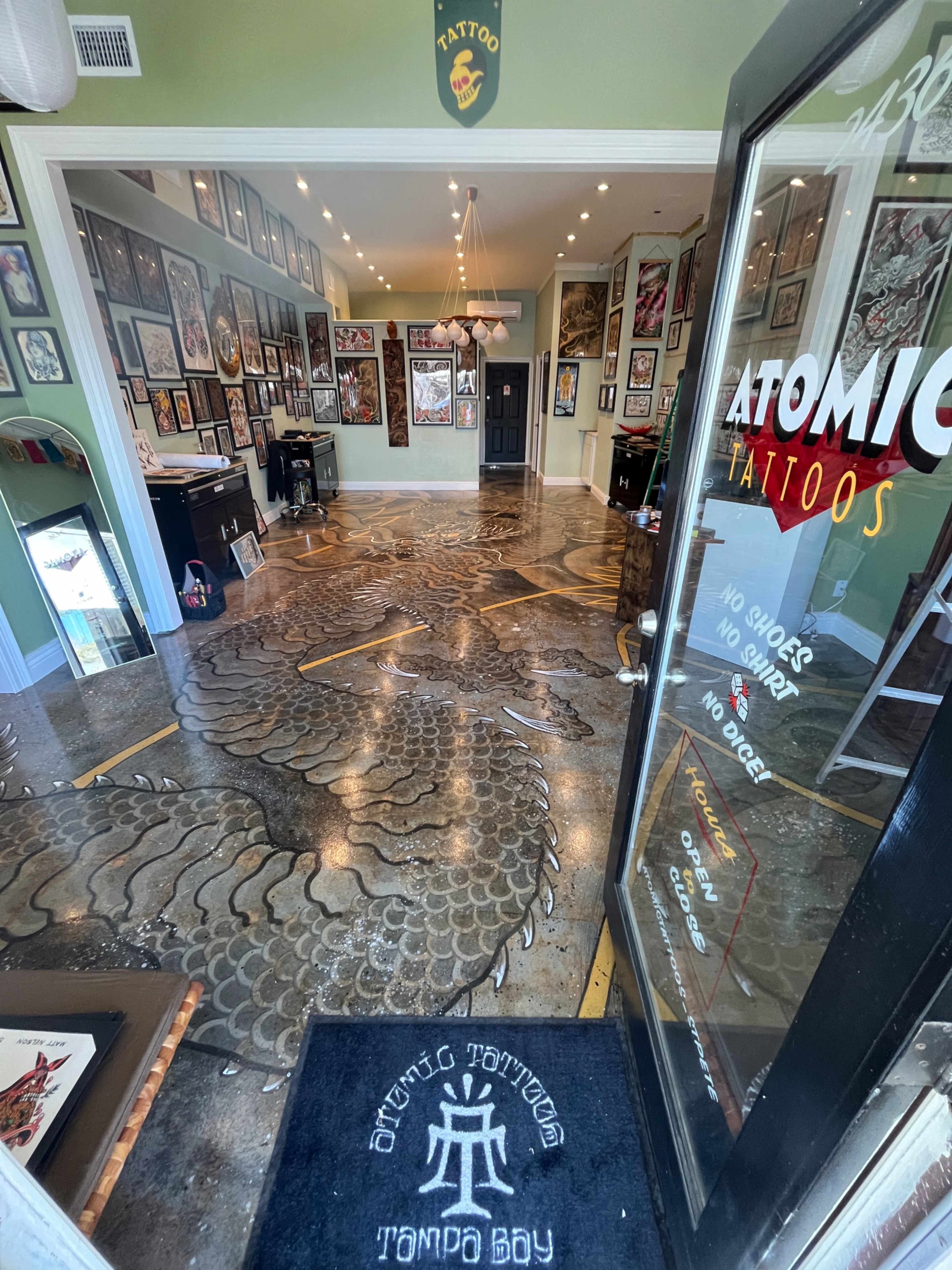 The image shows the interior of a tattoo shop with artworks displayed on the walls and a unique floor design.