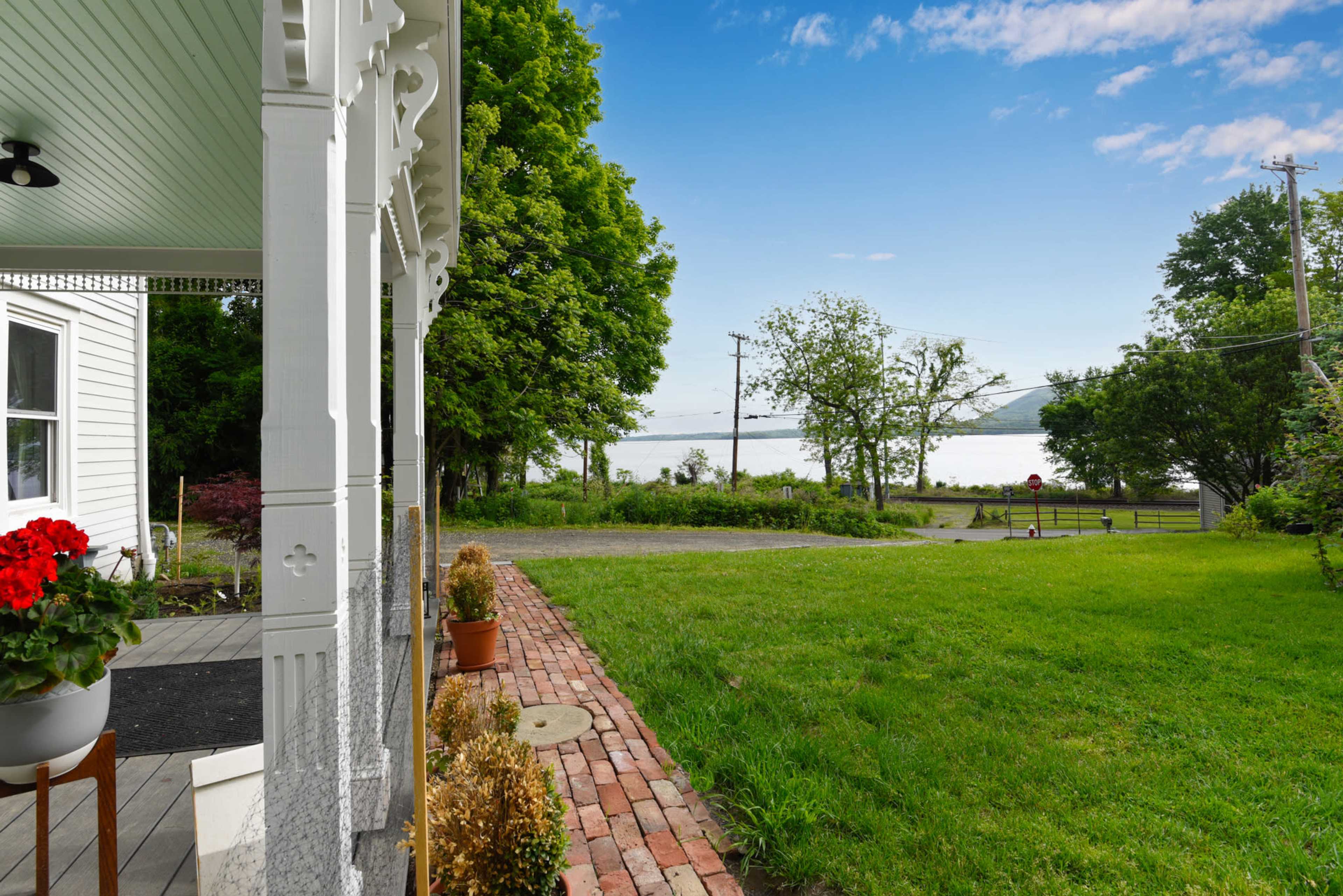 The image shows a view from a porch with a brick pathway leading to a grassy area and a lake visible in the distance, framed by trees.
