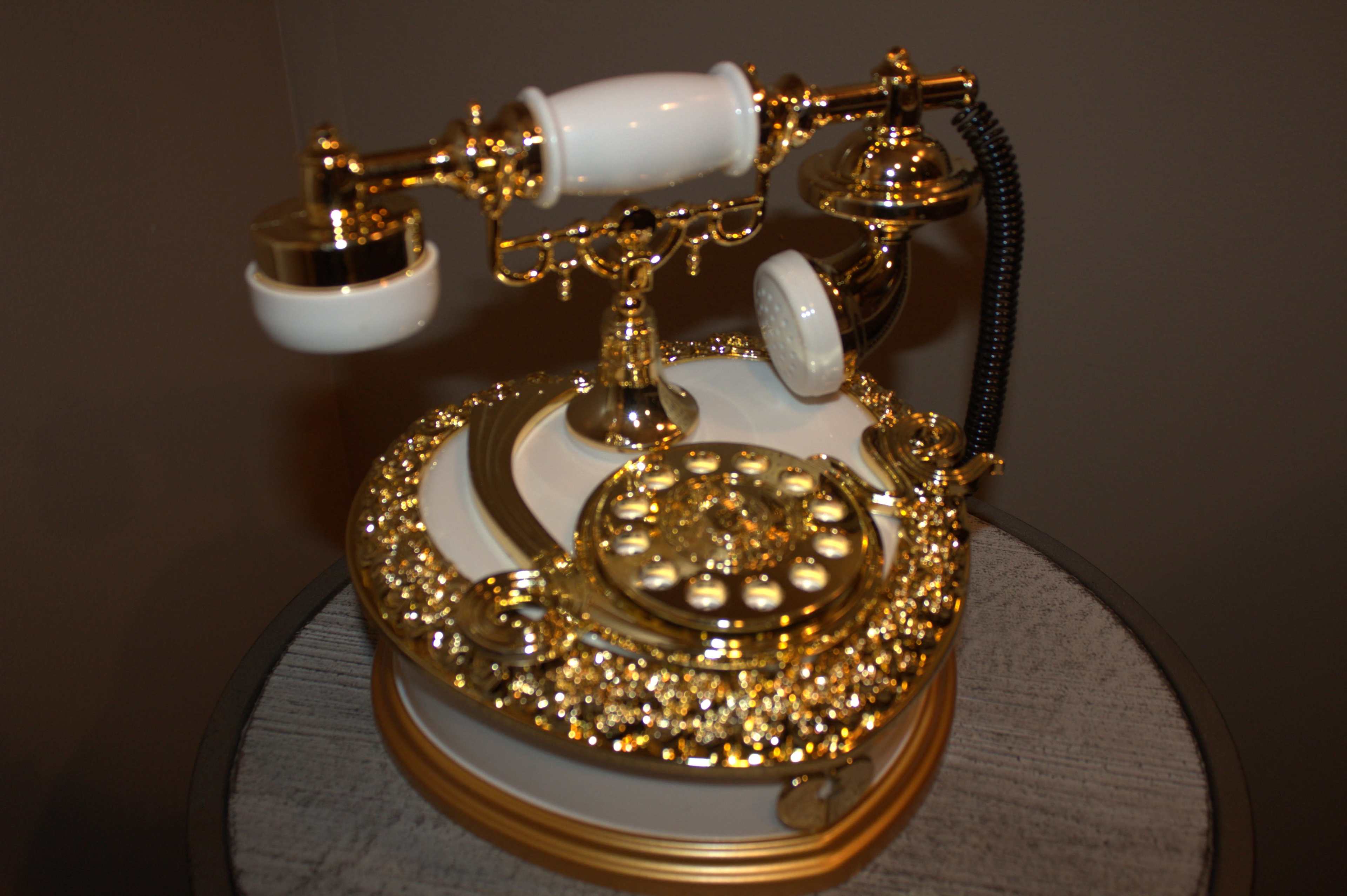 The image shows an ornate, vintage-style telephone with gold accents and a rotary dial set on a circular table.