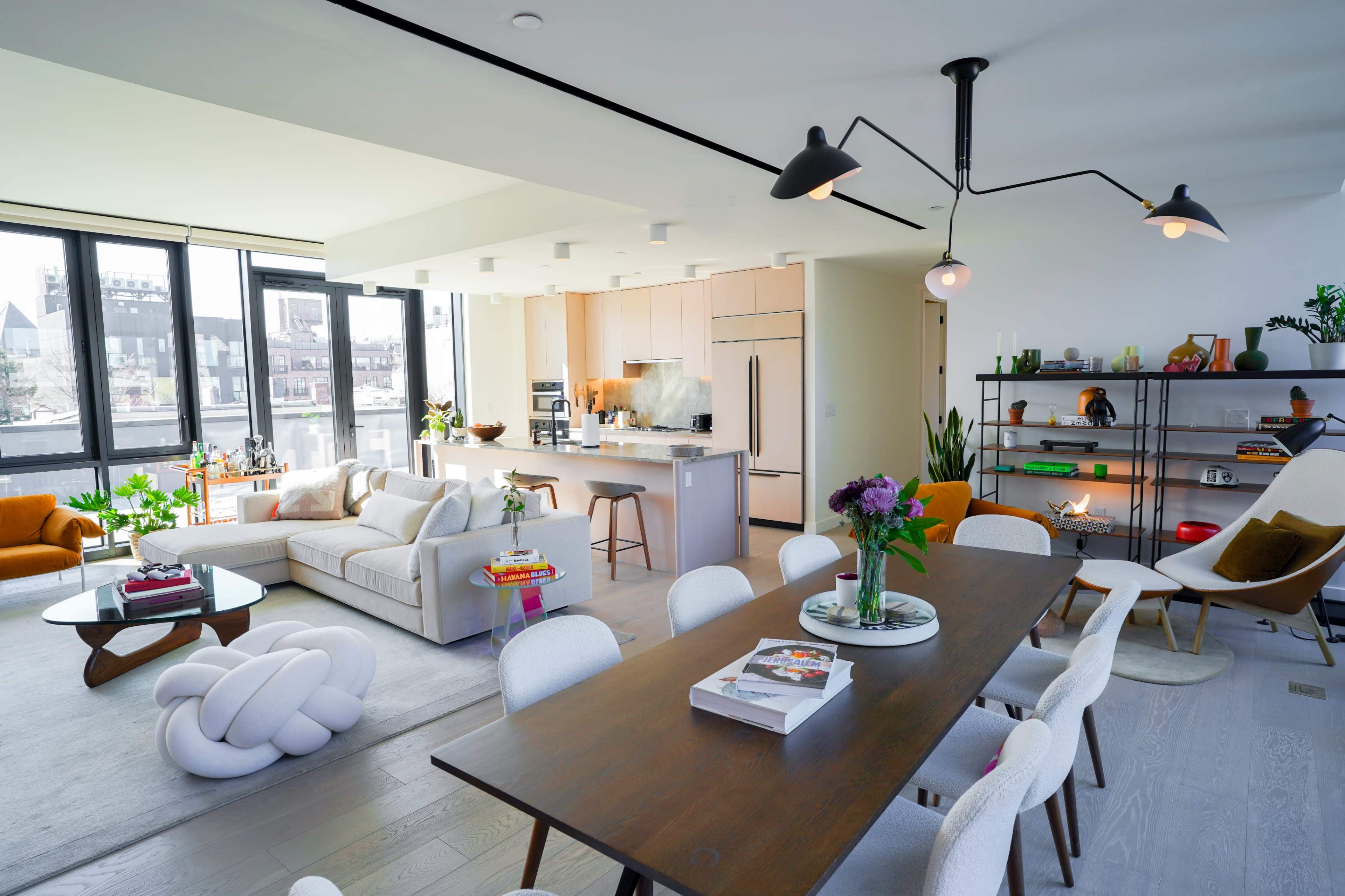 A modern open-concept living area featuring a seating area with a large sofa, dining table with chairs, and a kitchen in the background.