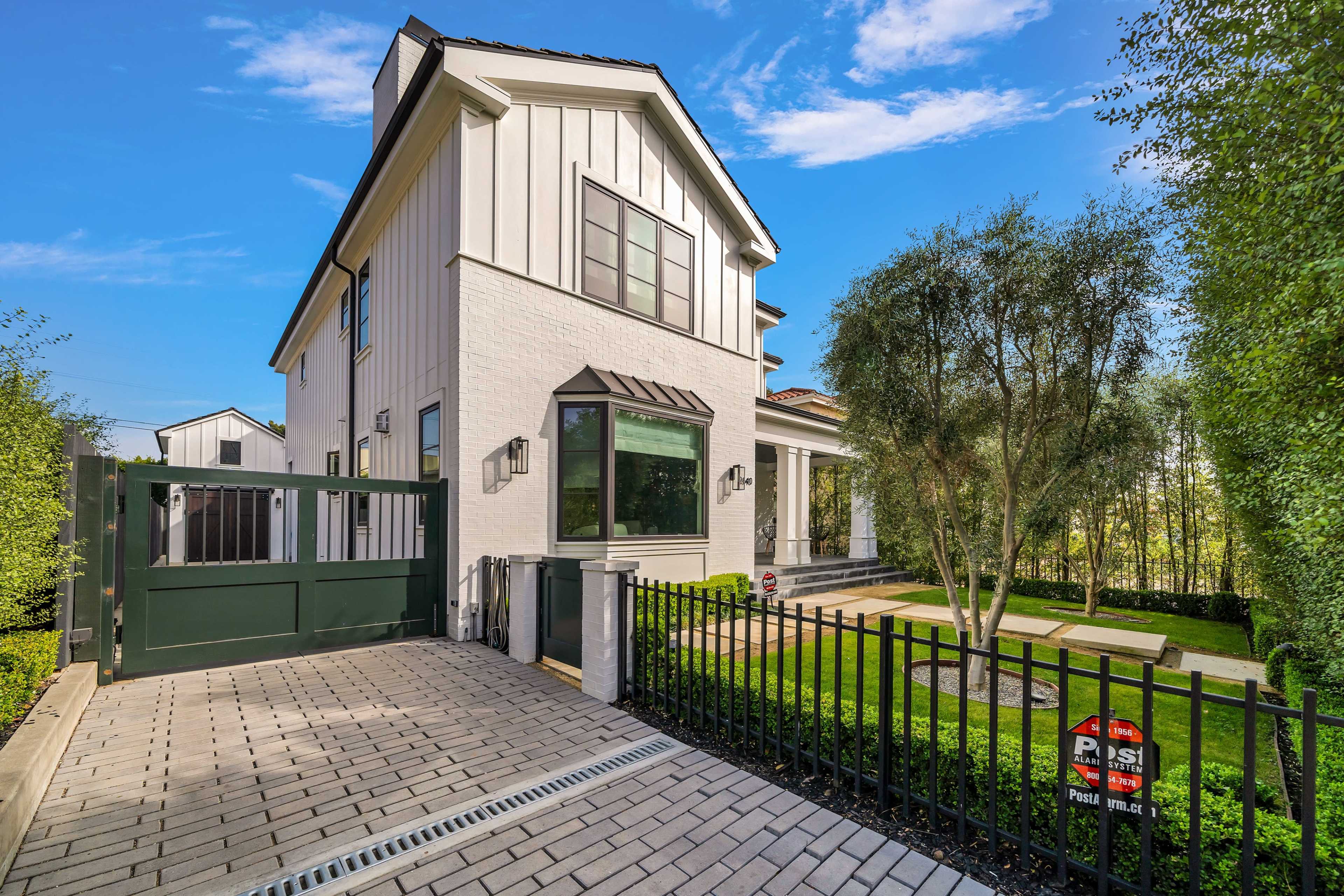 A modern two-story house with a white exterior and a green gate is situated in a landscaped area with a paved driveway.