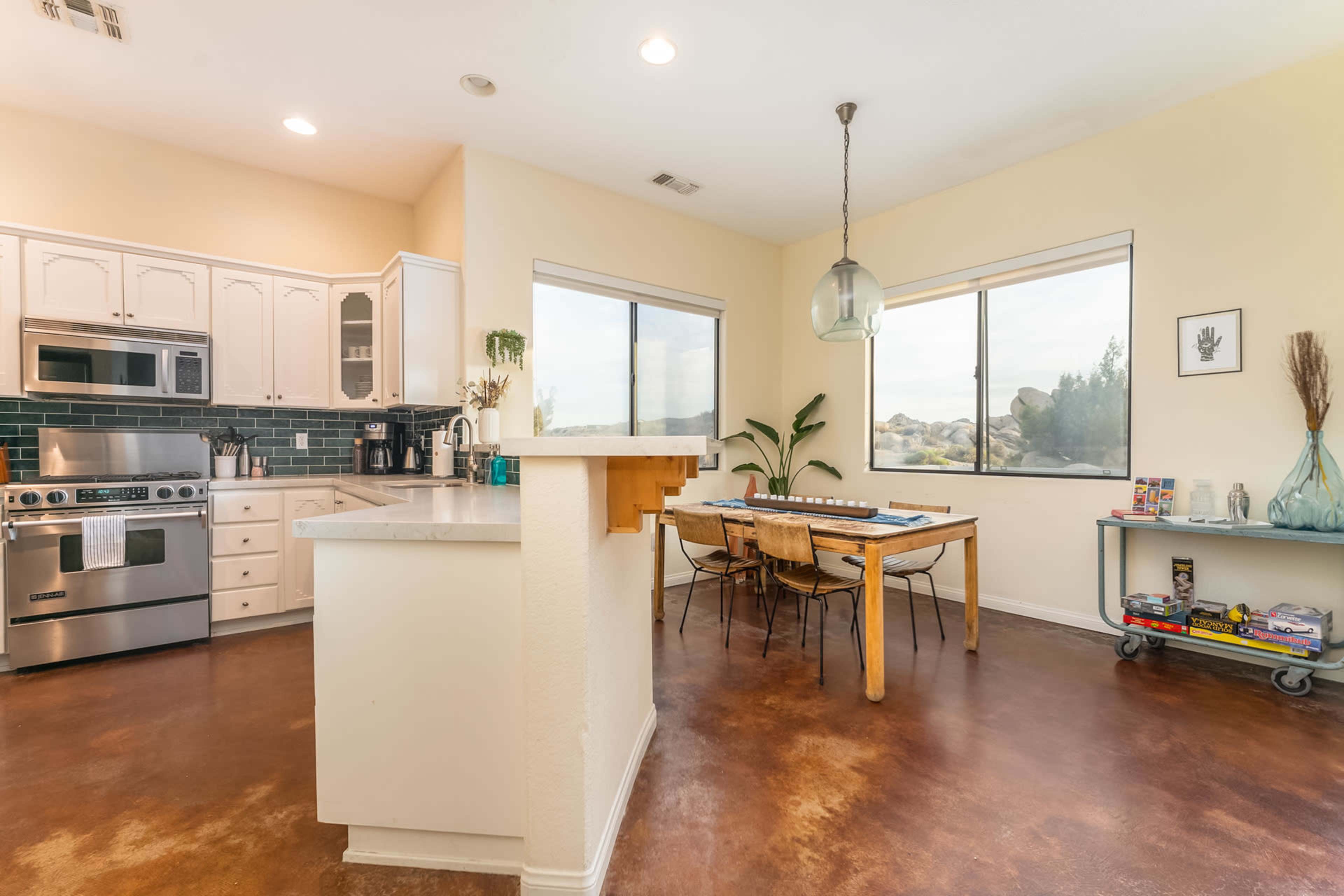 A modern kitchen with stainless steel appliances, a dining area featuring a wooden table and chairs, and large windows providing natural light.