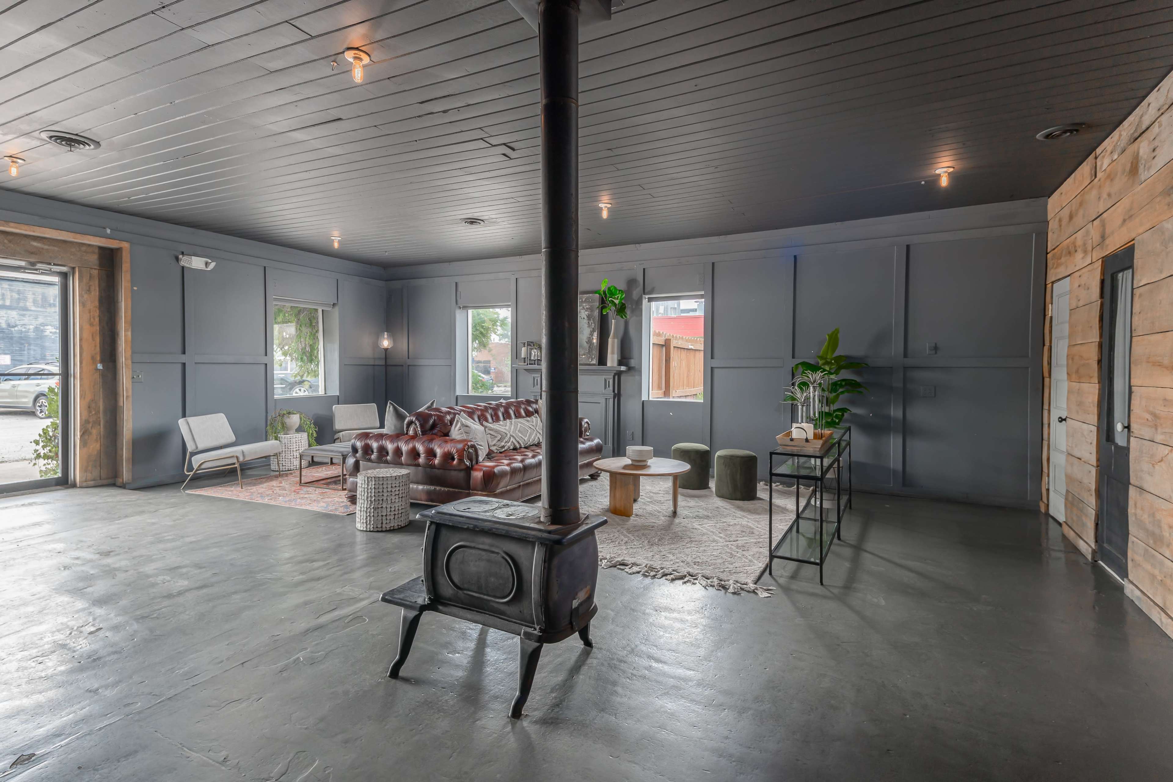 A spacious, modern interior with a leather sofa, a coffee table arrangement, and a wood stove in the center.