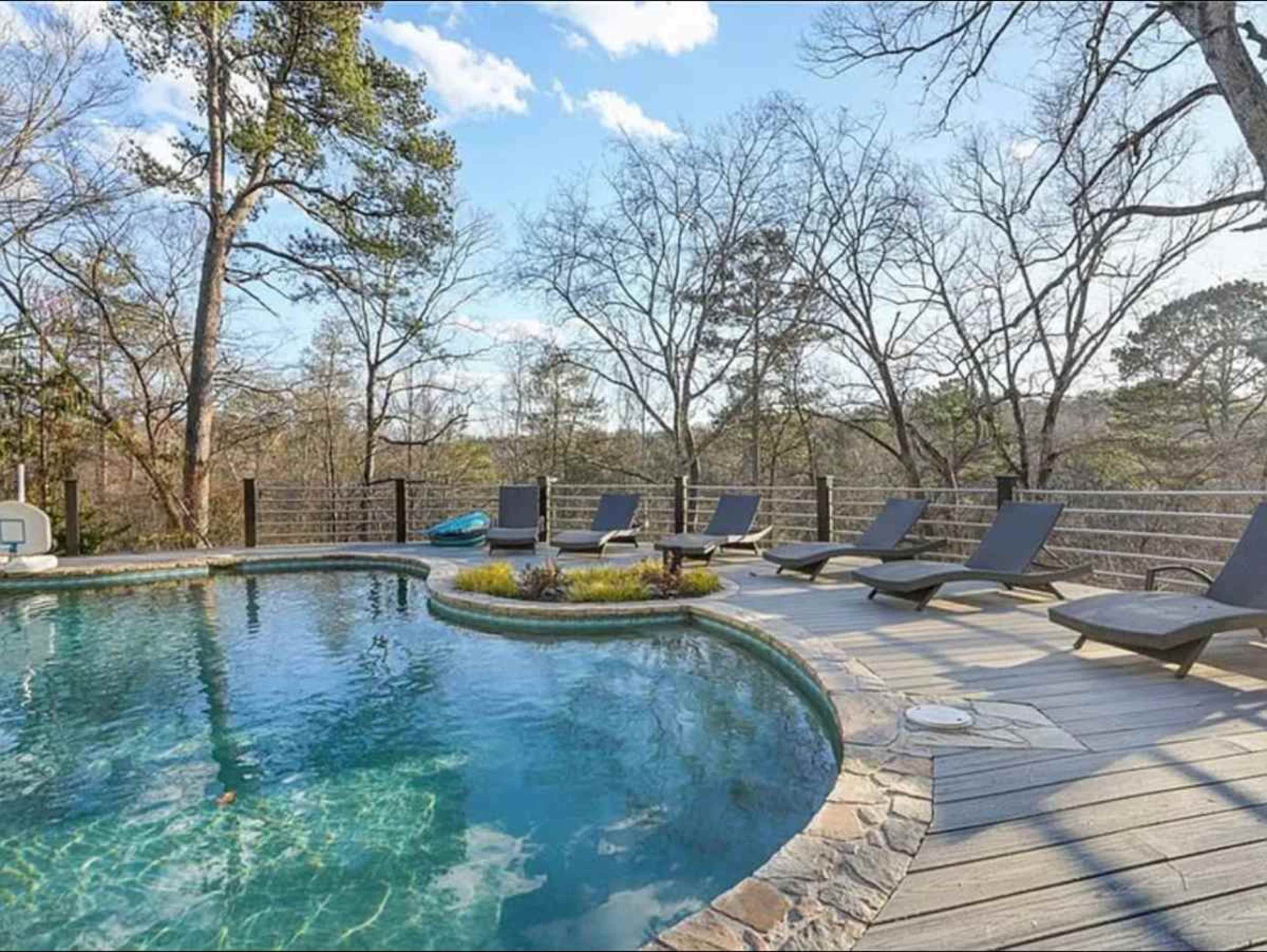 A swimming pool with a stone border, surrounded by lounge chairs and set against a backdrop of bare trees and clear blue skies.