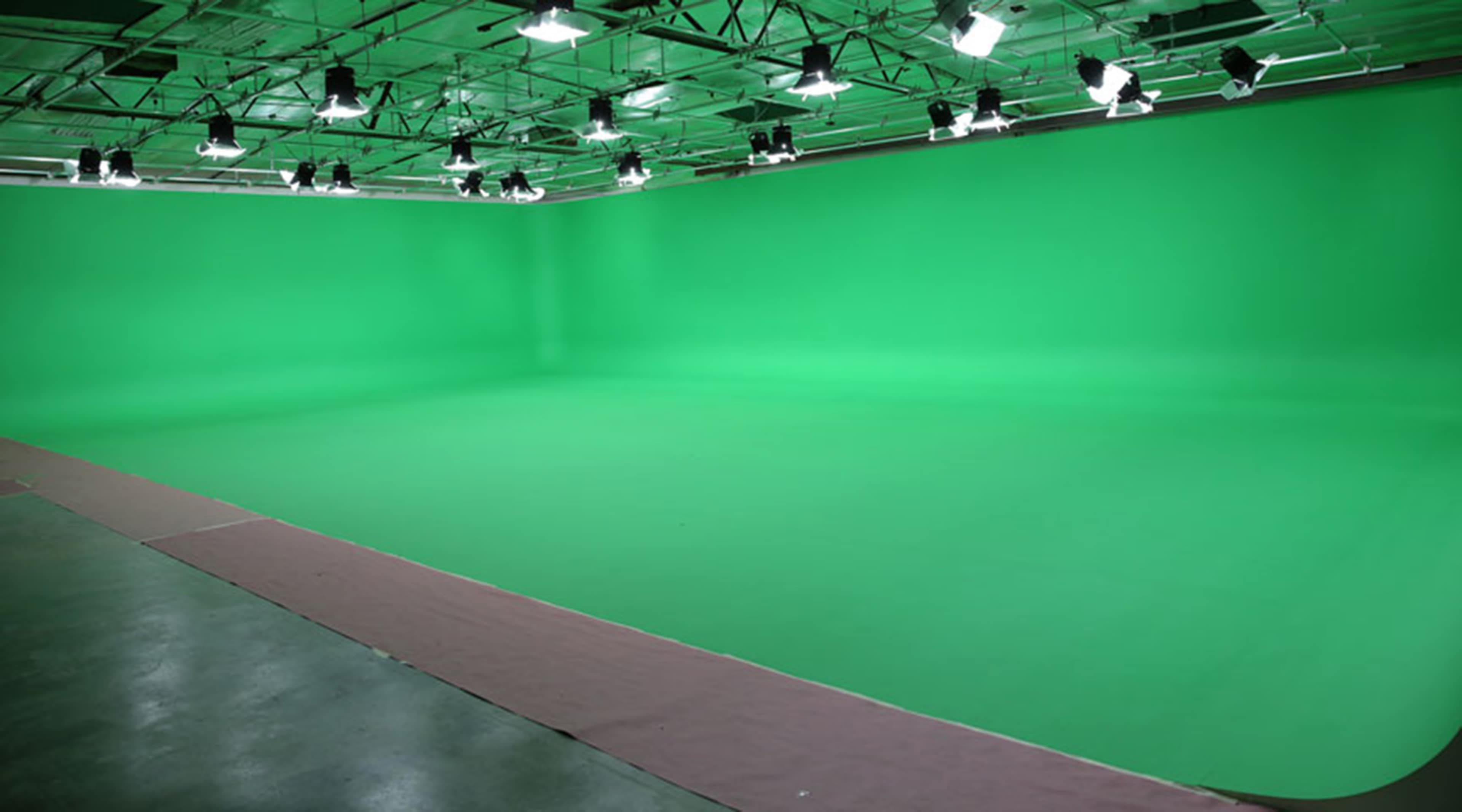 A large green screen studio with bright lights set up overhead.
